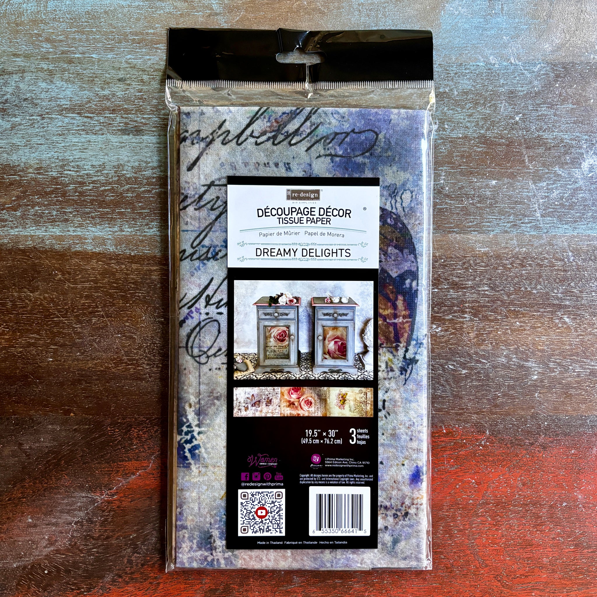 A package of ReDesign with Prima's Dreamy Delights tissue paper 3 pack is against a dark wood background.