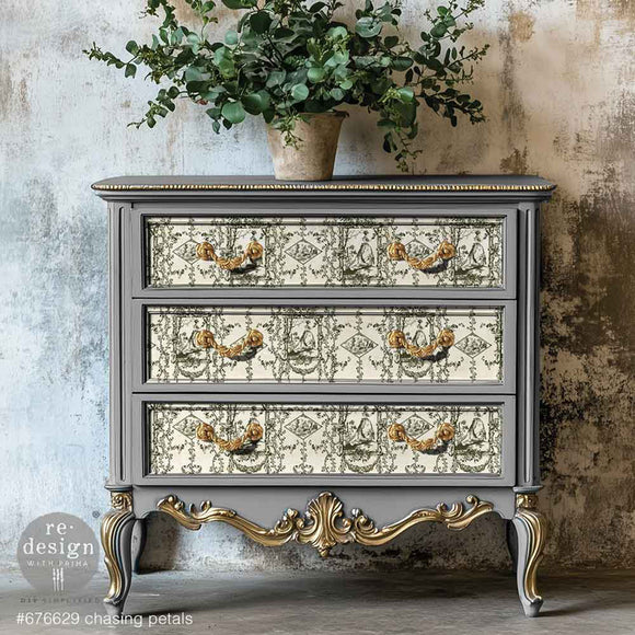 A vintage 3-drawer chest dresser is painted grey with gold accents and features ReDesign with Prima's KACHA Chasing Petals fiber paper on the drawers. 