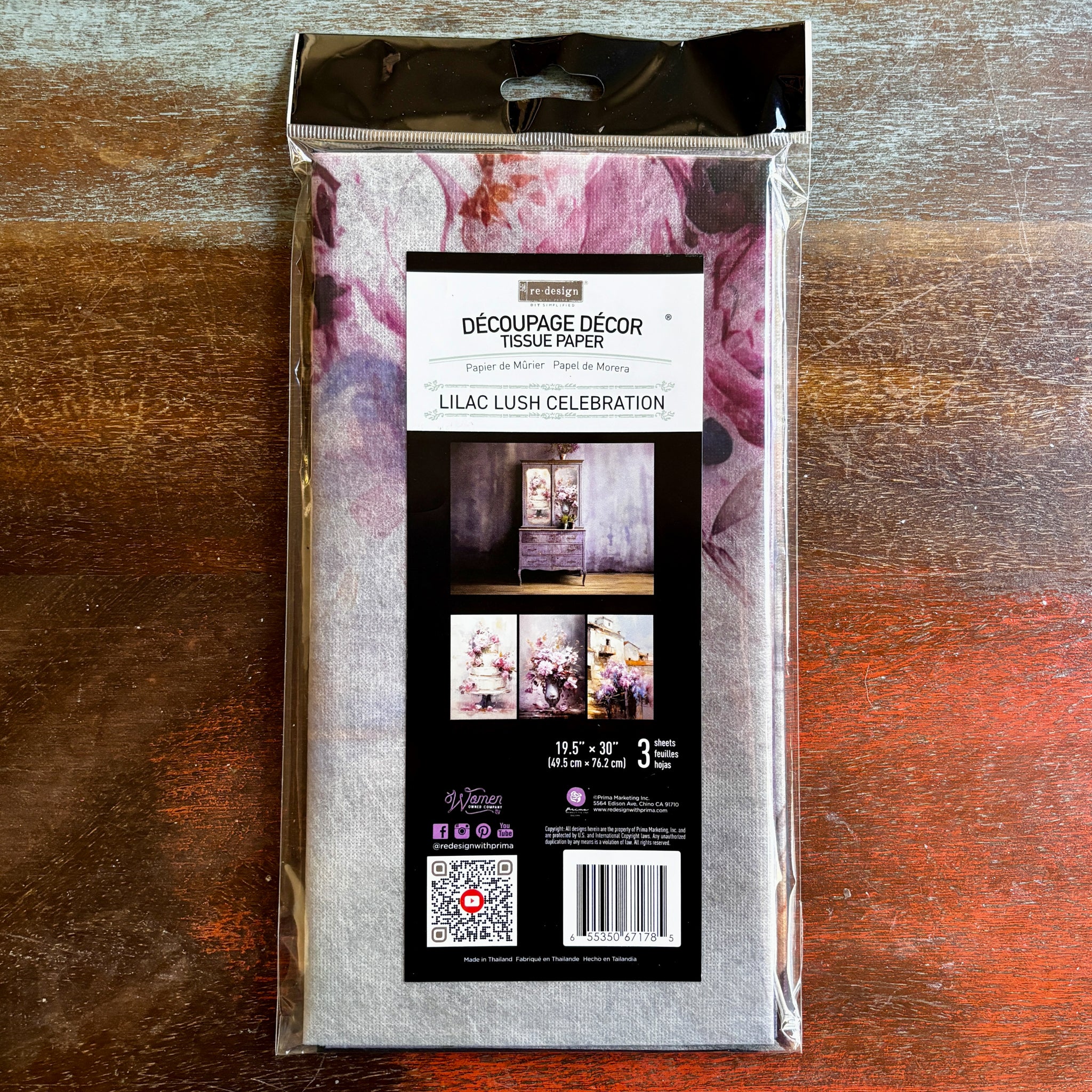 A package of ReDesign with Prima's Lilac Lush Celebration tissue paper is against a dark wood background.