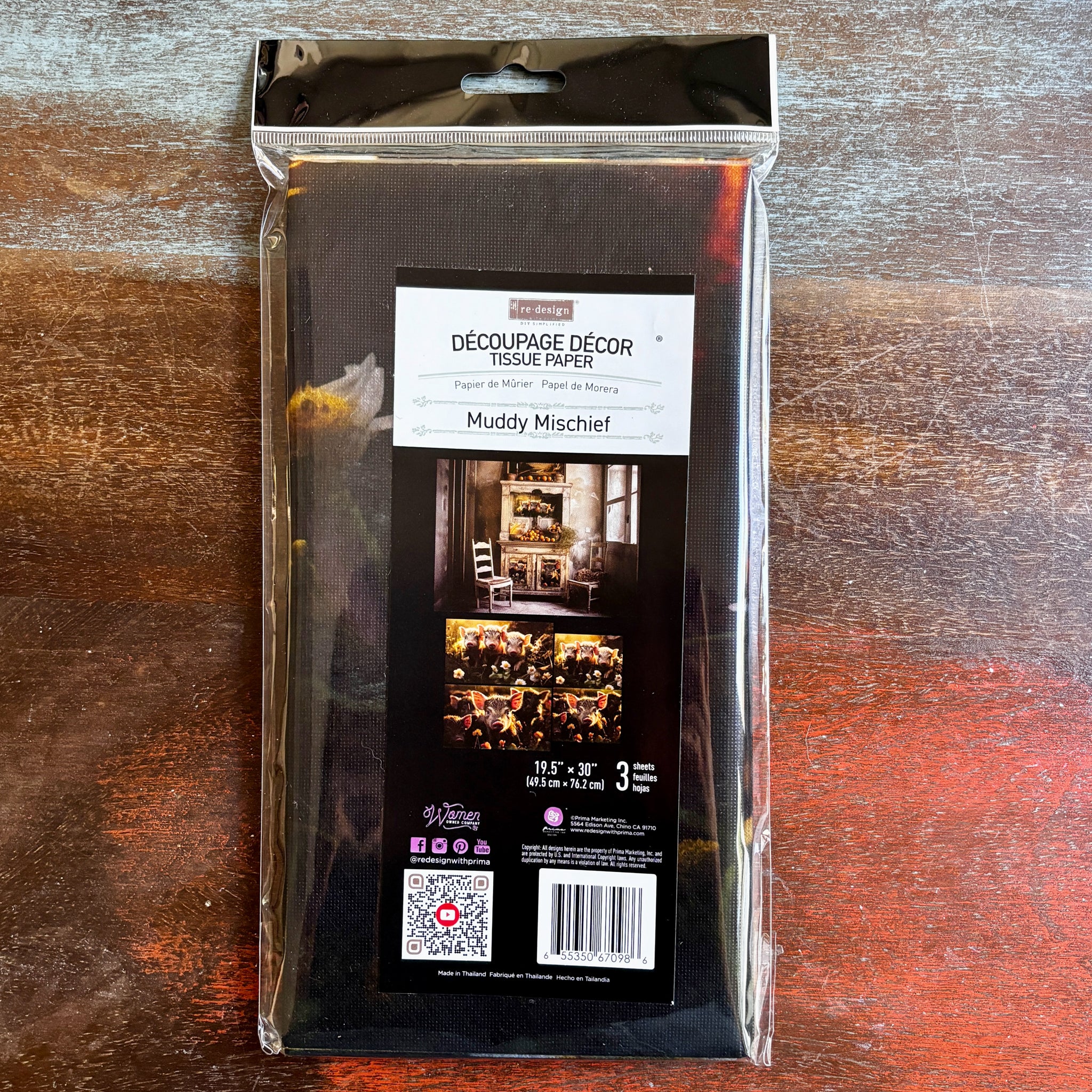 A package of ReDesign with Prima's Muddy Mischief tissue paper is against a dark wood background.