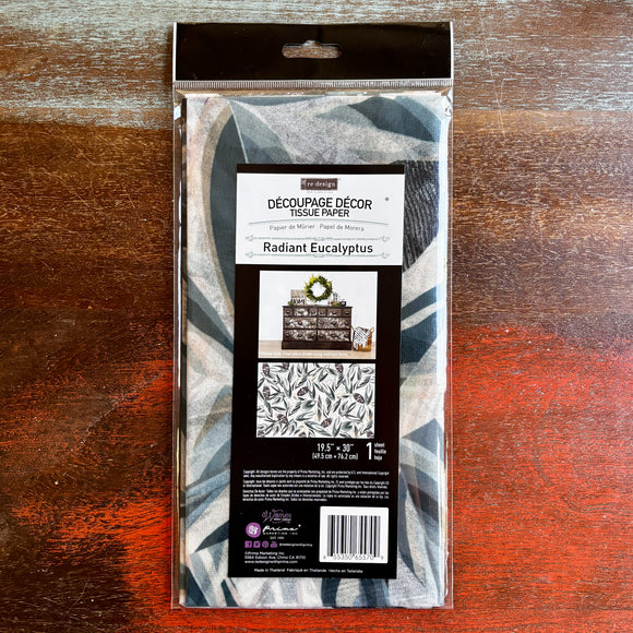 A package of ReDesign with Prima's Radiant Eucalyptus tissue paper is against a dark wood background.