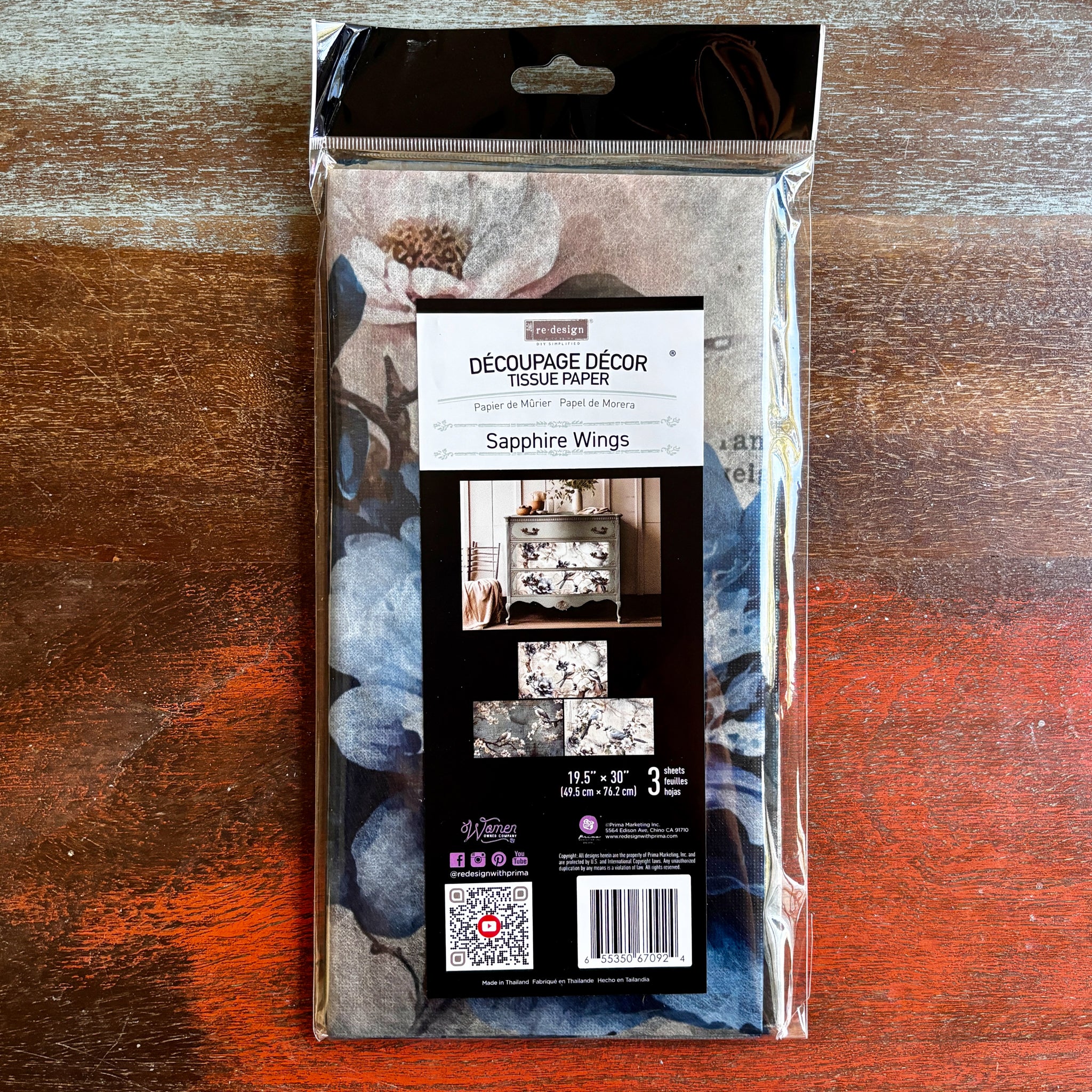 A package of ReDesign with Prima's Sapphire Wings tissue paper is against a dark wood background.