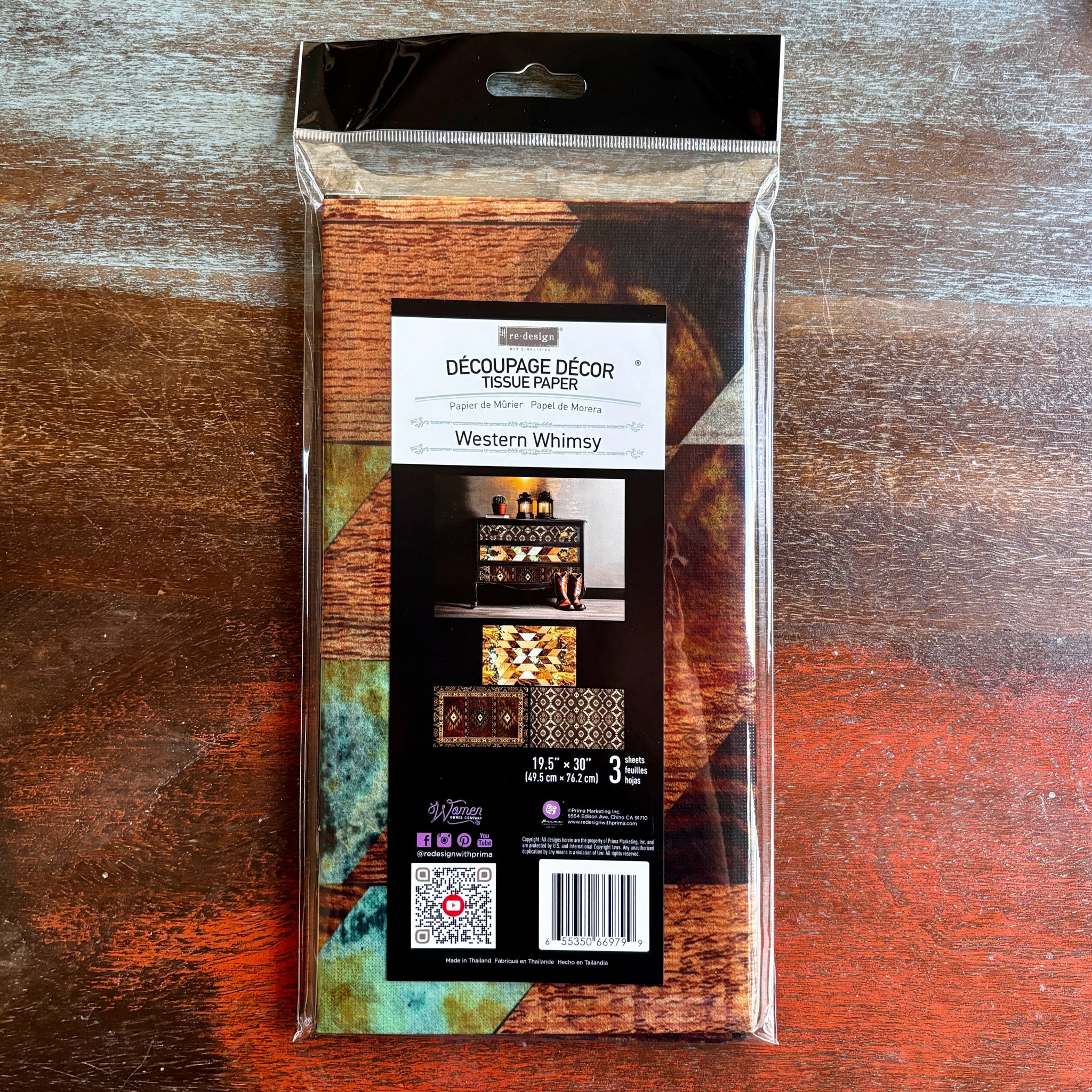 A package of ReDesign with Prima's Western Whimsy tissue paper is against a dark wood background.