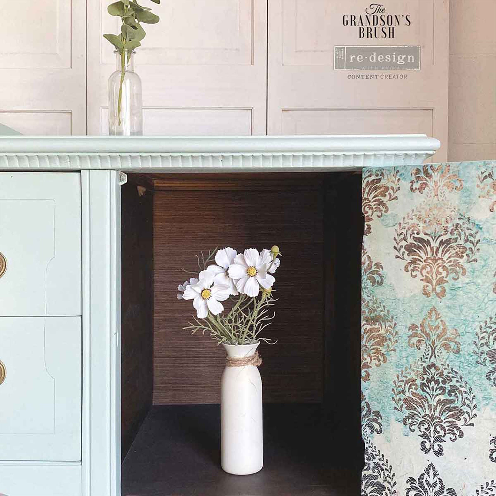 A close-up of a vintage console table with storage refurbished by The Grandson's Brush is painted pale blue and features ReDesign with Prima's Patina Flourish tissue paper inside of of the storage doors.