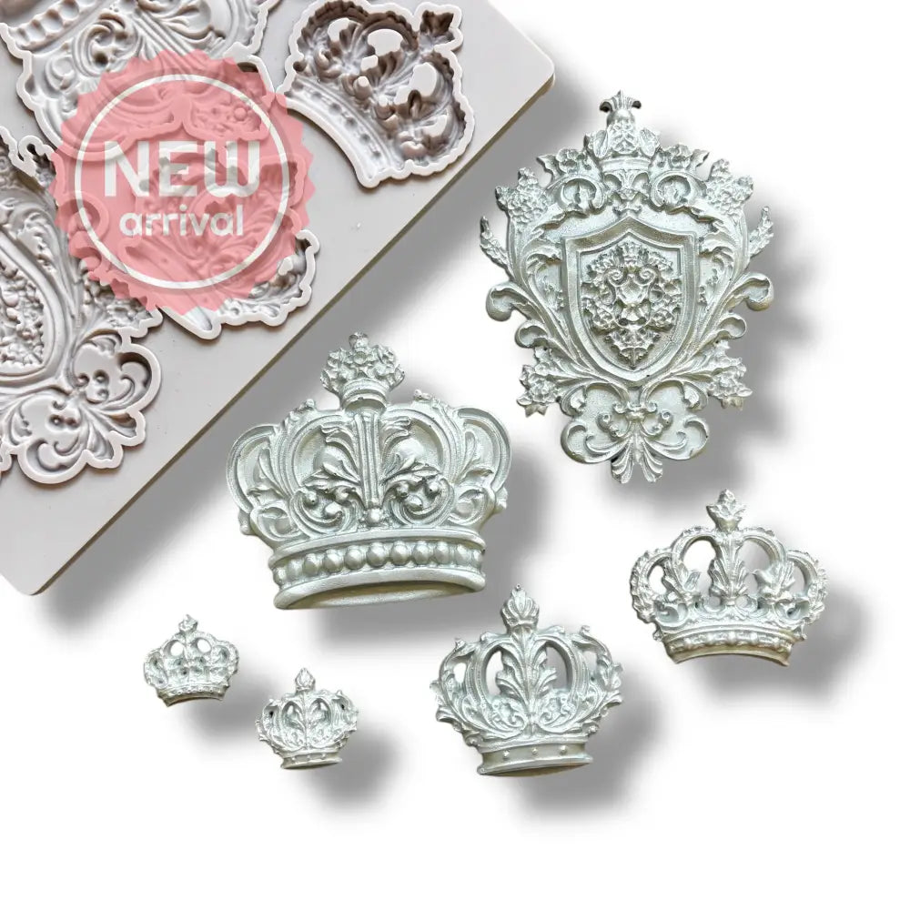 A light grey silicone mold and silver colored castings of 5 varying size regal crowns and a family crest are against a white background.