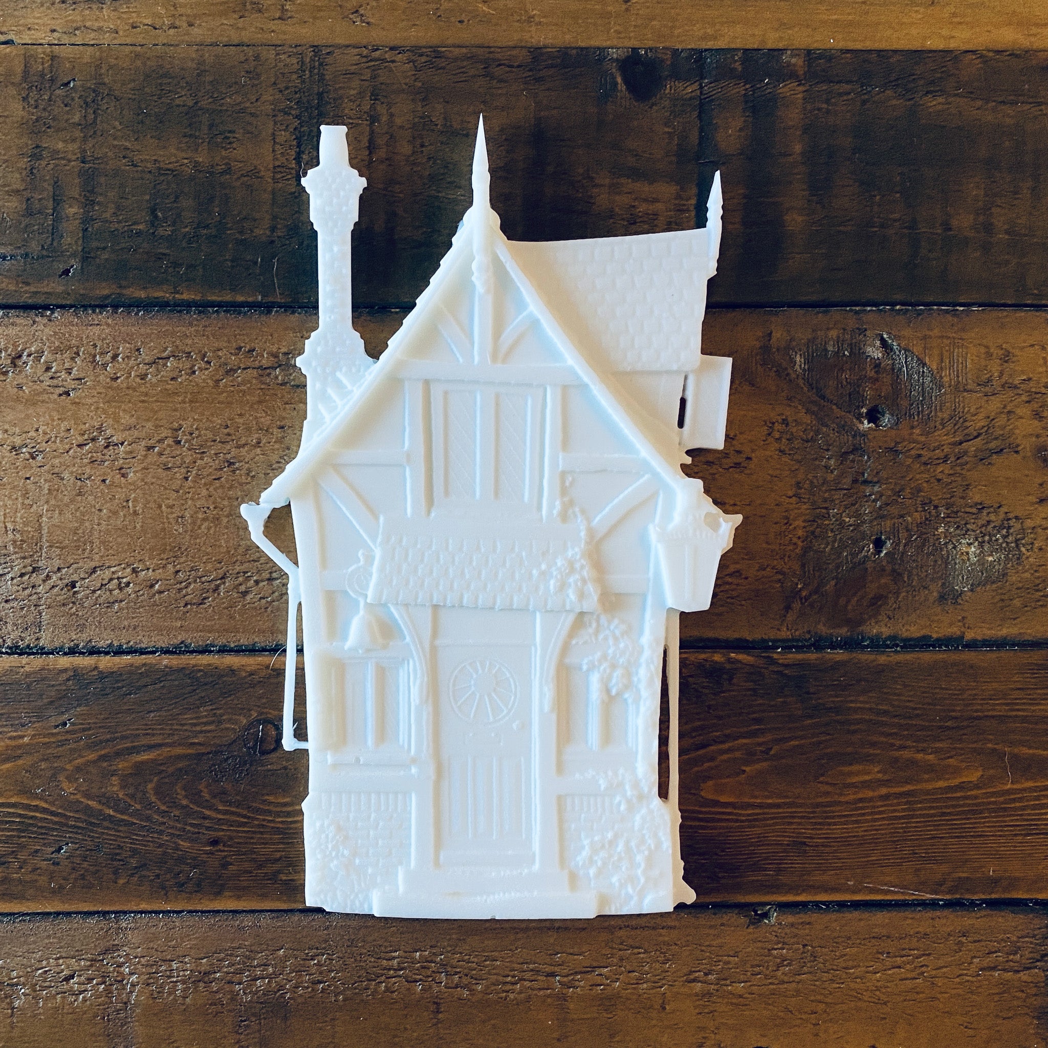 A white resin silicone mold casting of a small Victorian style fairy house is against a wood background.