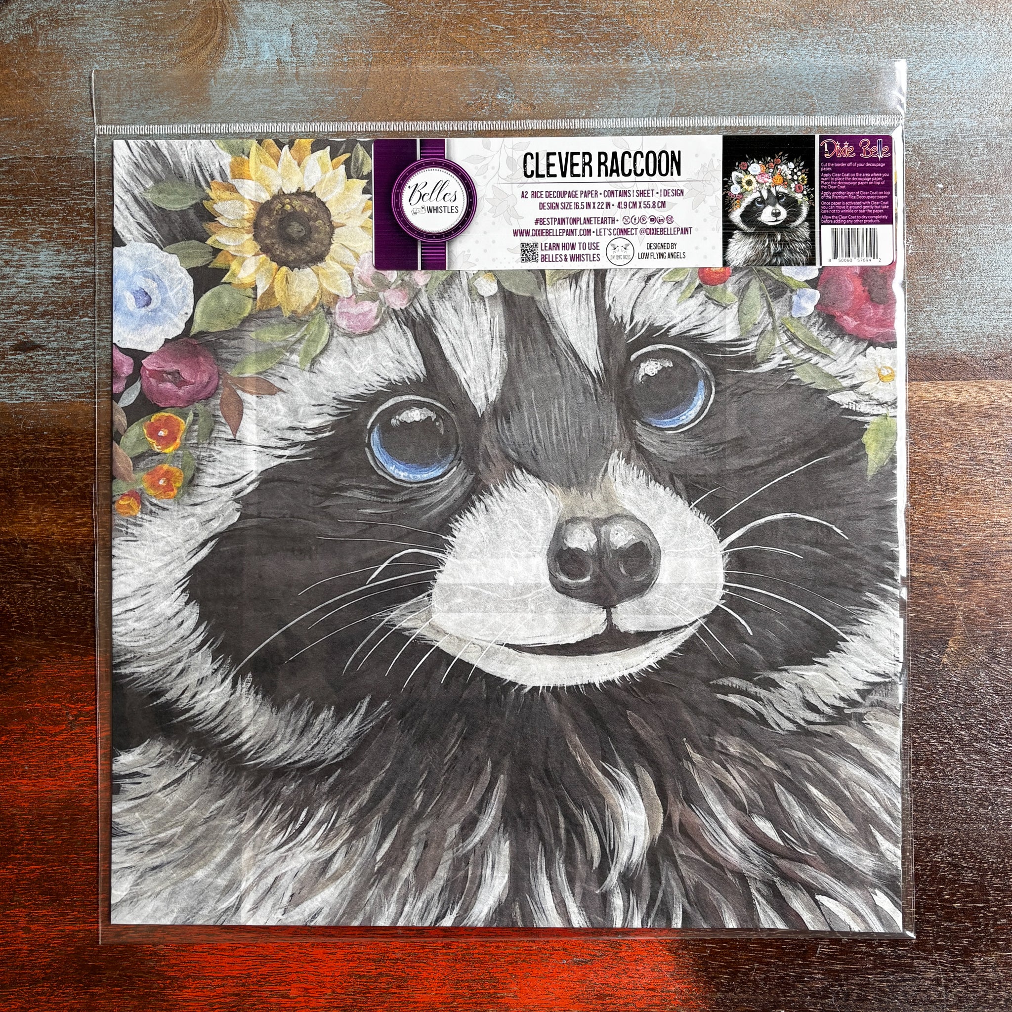 A package of Belles & Whistles' Clever Raccoon A2 rice paper is against a dark wood background.