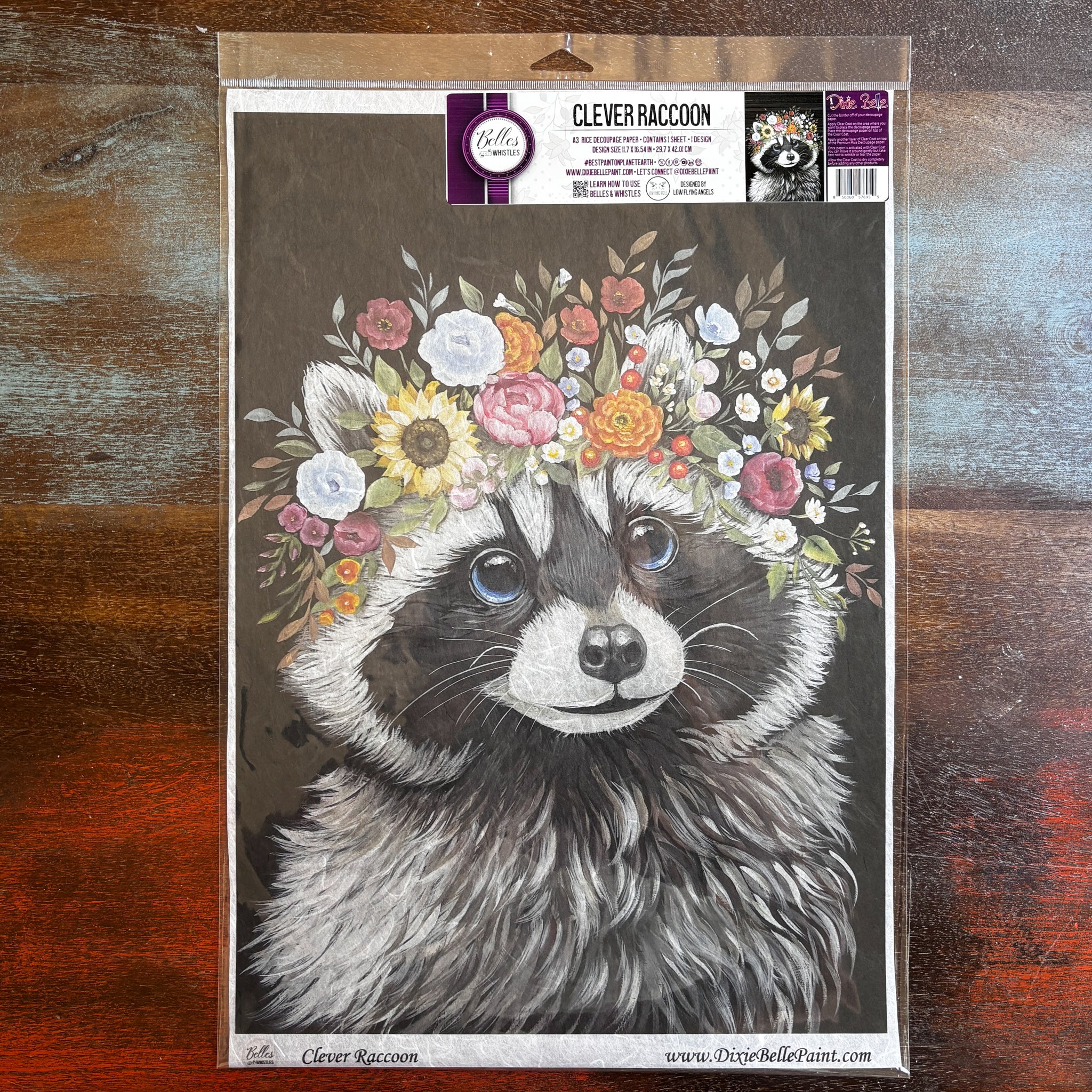 A package of Belles & Whistles' Clever Raccoon A3 rice paper is against a dark wood background.