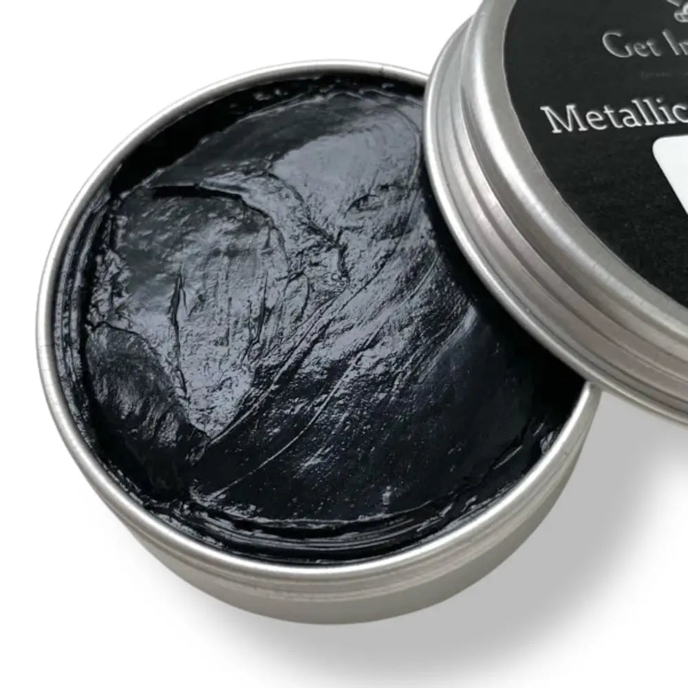 A close-up of a 0.70 (20 ml) open container of a black metallic wax mousse paste is against a white background.