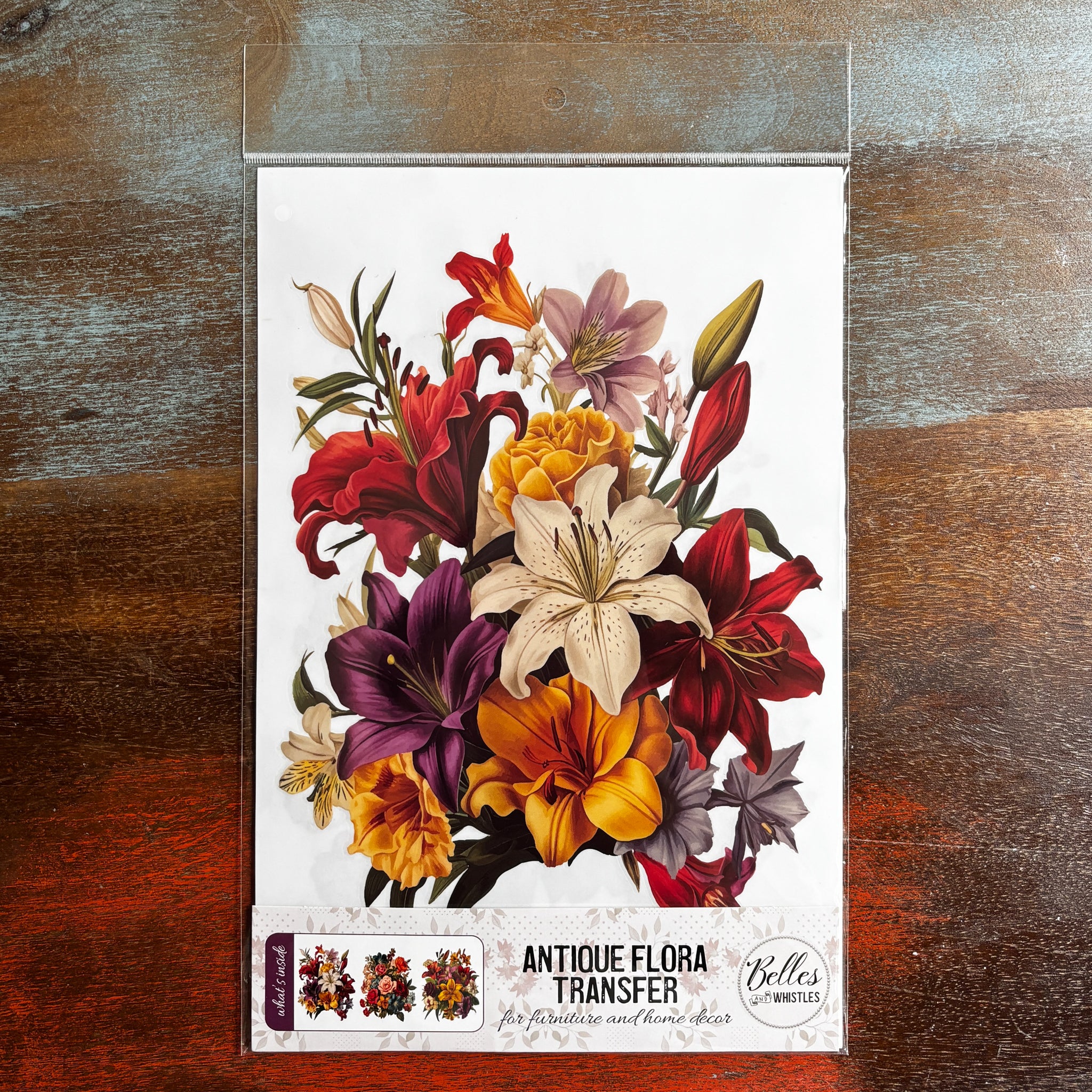 A package of Belles & Whistles' Antique Flora rub-on transfer is against a dark wood background.