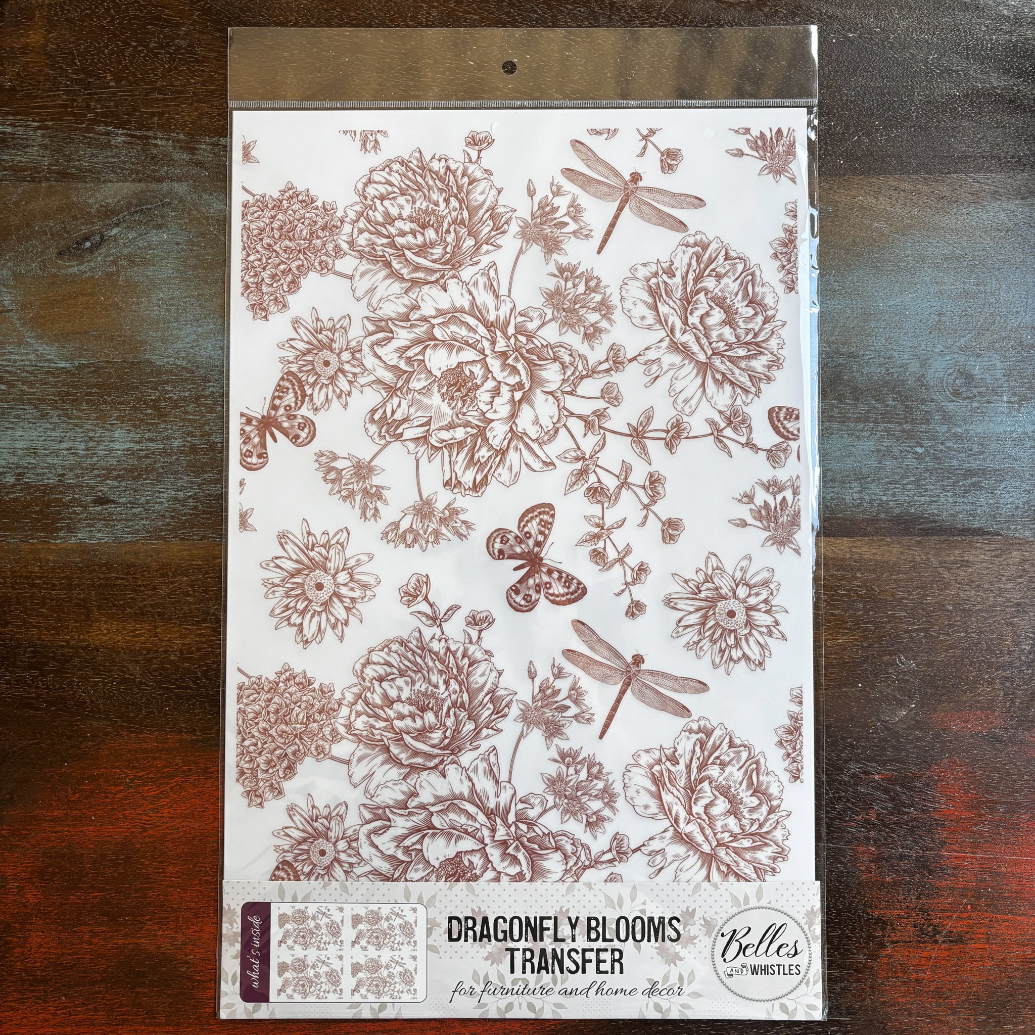 A package of Belles & Whistles' Dragonfly Blooms rub-on transfer is against a dark wood background.