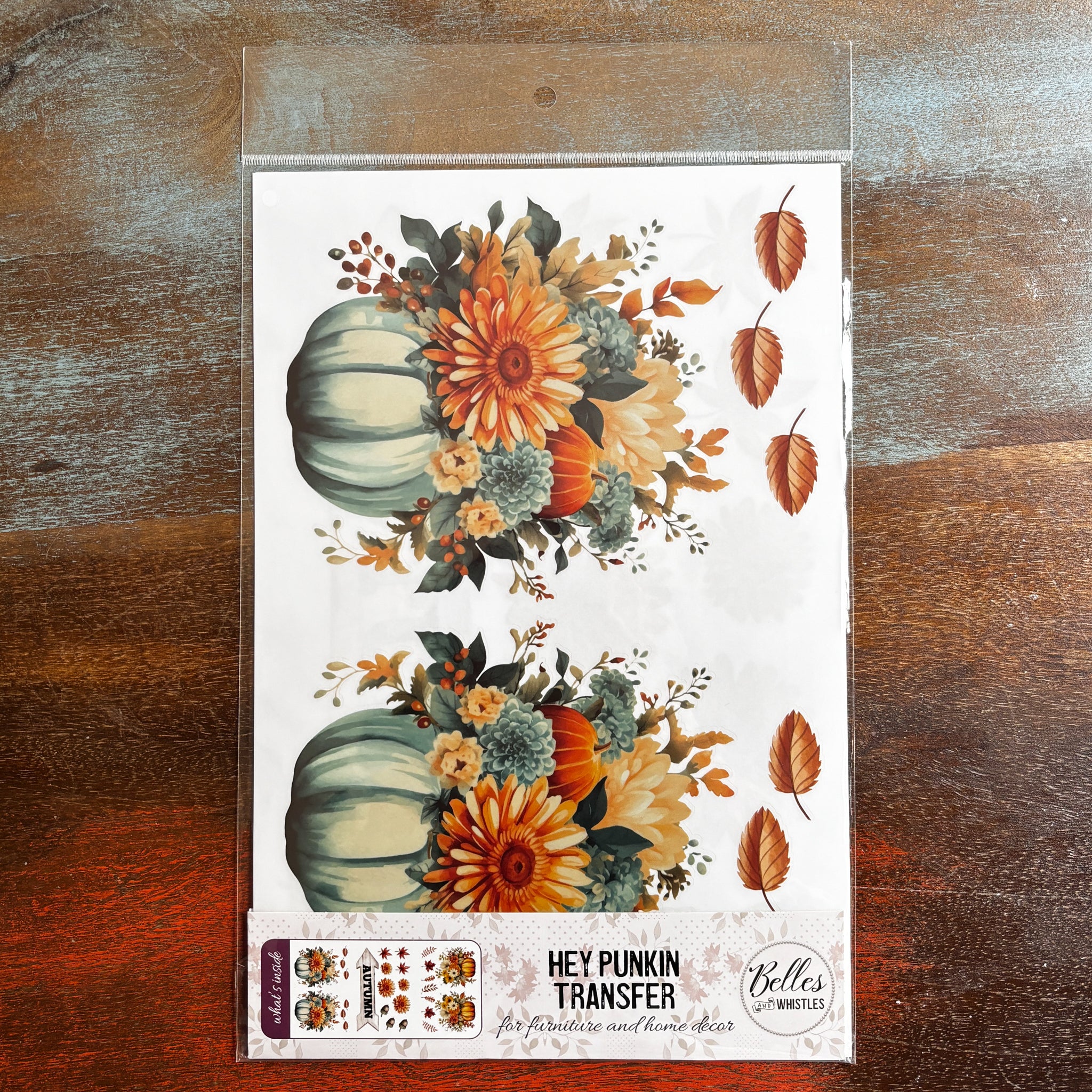 A package of Belles & Whistles' Hey Punkin rub-on transfer is against a dark wood background.