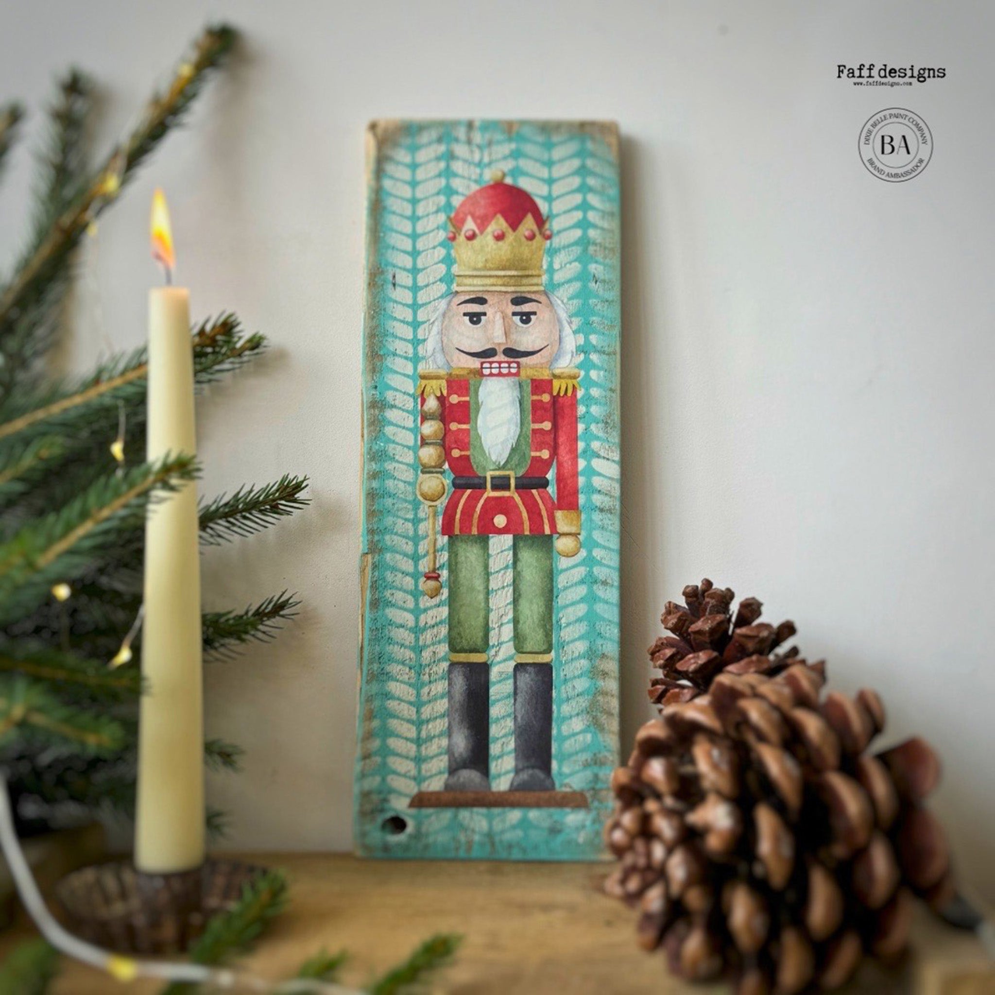 A tall woodcraft project painted teal with a pattern by Faff Designs features a nutcracker in a red crown and jacket from Belles & Whistles' Nutcracker small rub-on transfer on it.