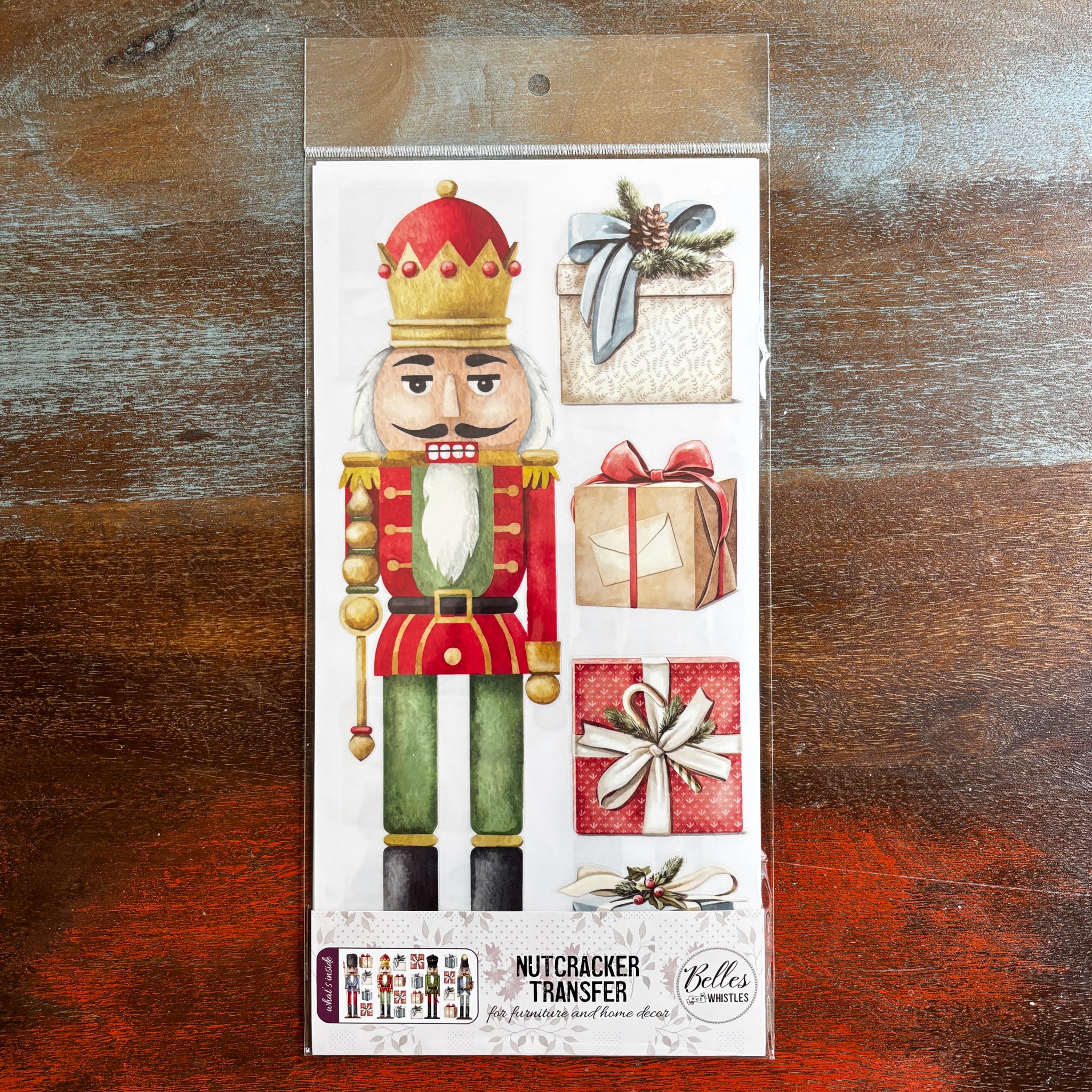 A package of Belles & Whistles' Nutcracker rub-on transfer is against a dark wood background.