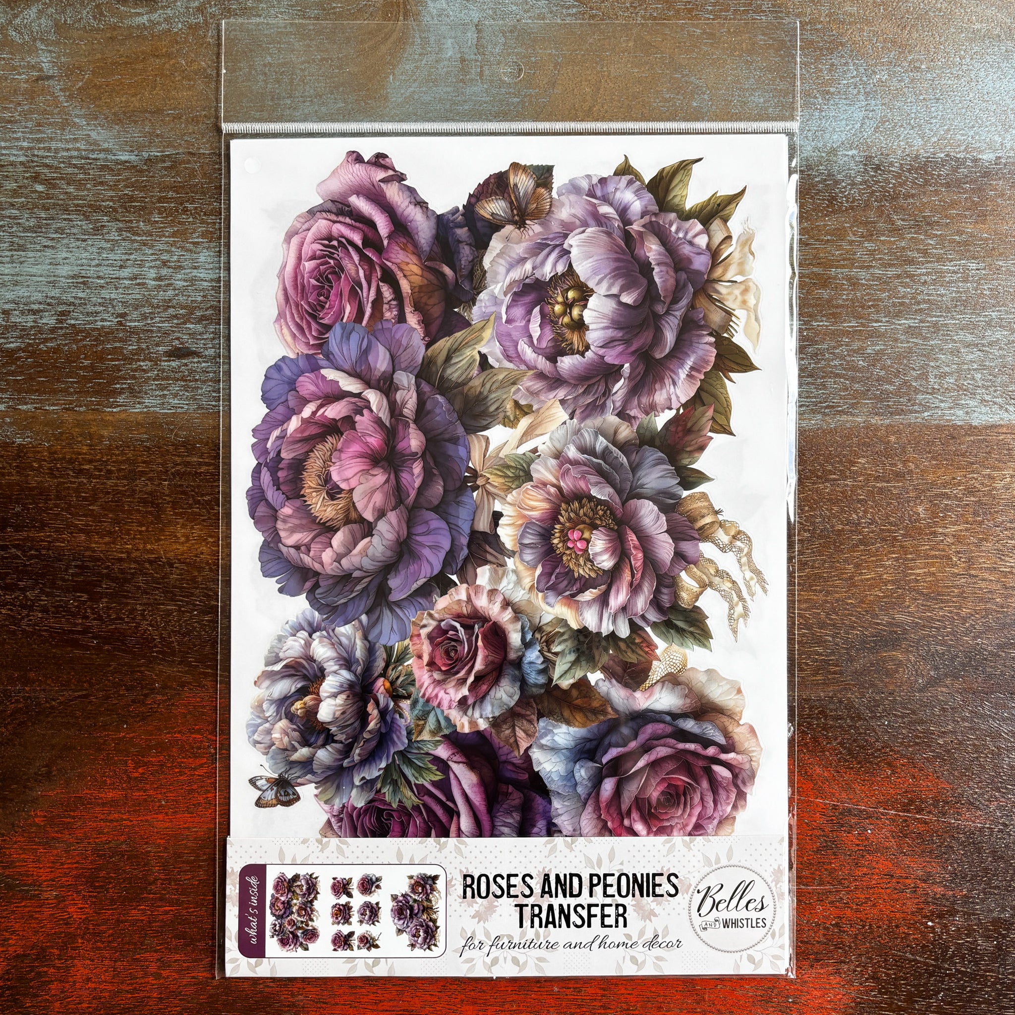 A package of Belles & Whistles'  Roses and Peonies rub-on transfer is against a dark wood background.