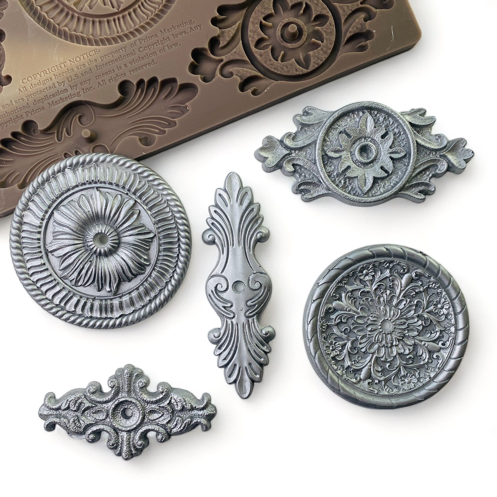 Silver colored silicone mold castings of 5 ornate drawer pull plates are against a white background.