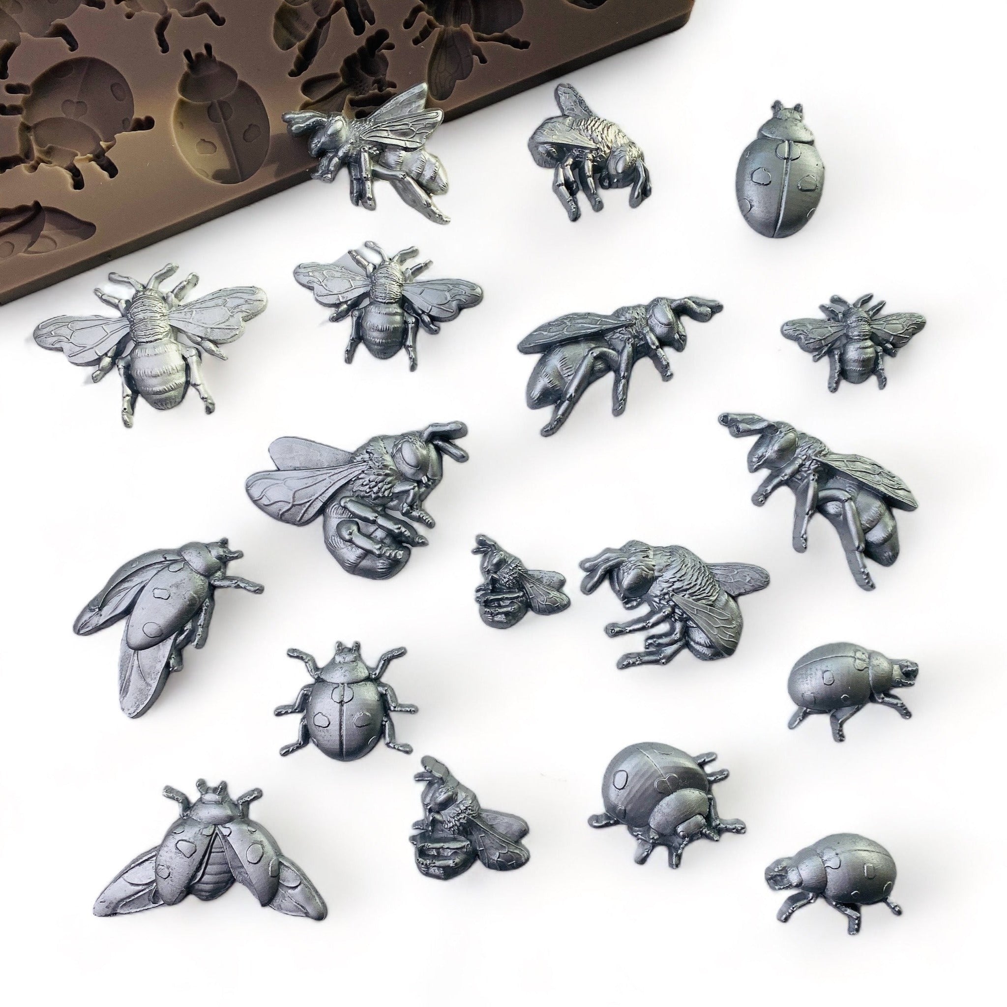Silver colored silicone mold castings of 18 bees and ladybugs are against a white background.