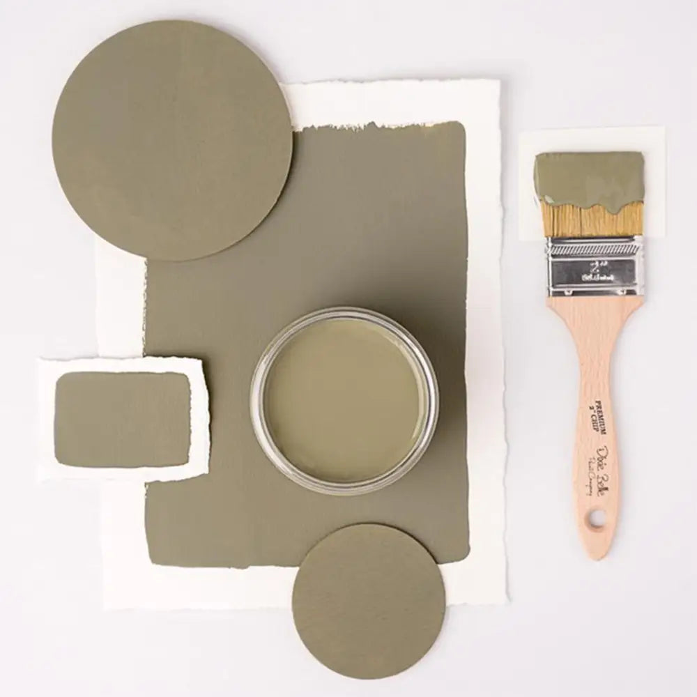 A paint brush, paper, and round wood samples of Dixie Belle's Thicket Chalk Mineral Paint are against a white background.