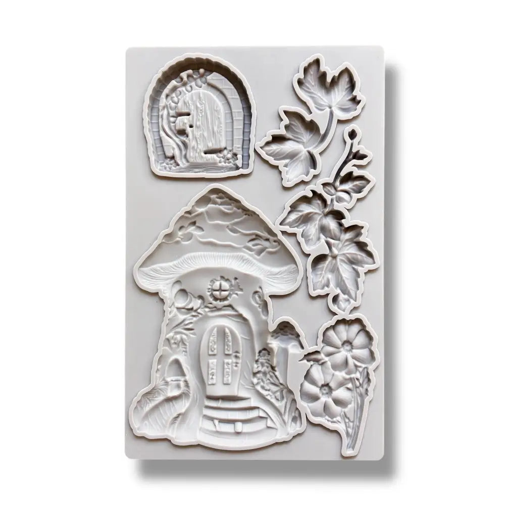 A light grey silicone mold featuring a mushroom fairy house, a hobbit style door, and leaves and flowers is against a white background.