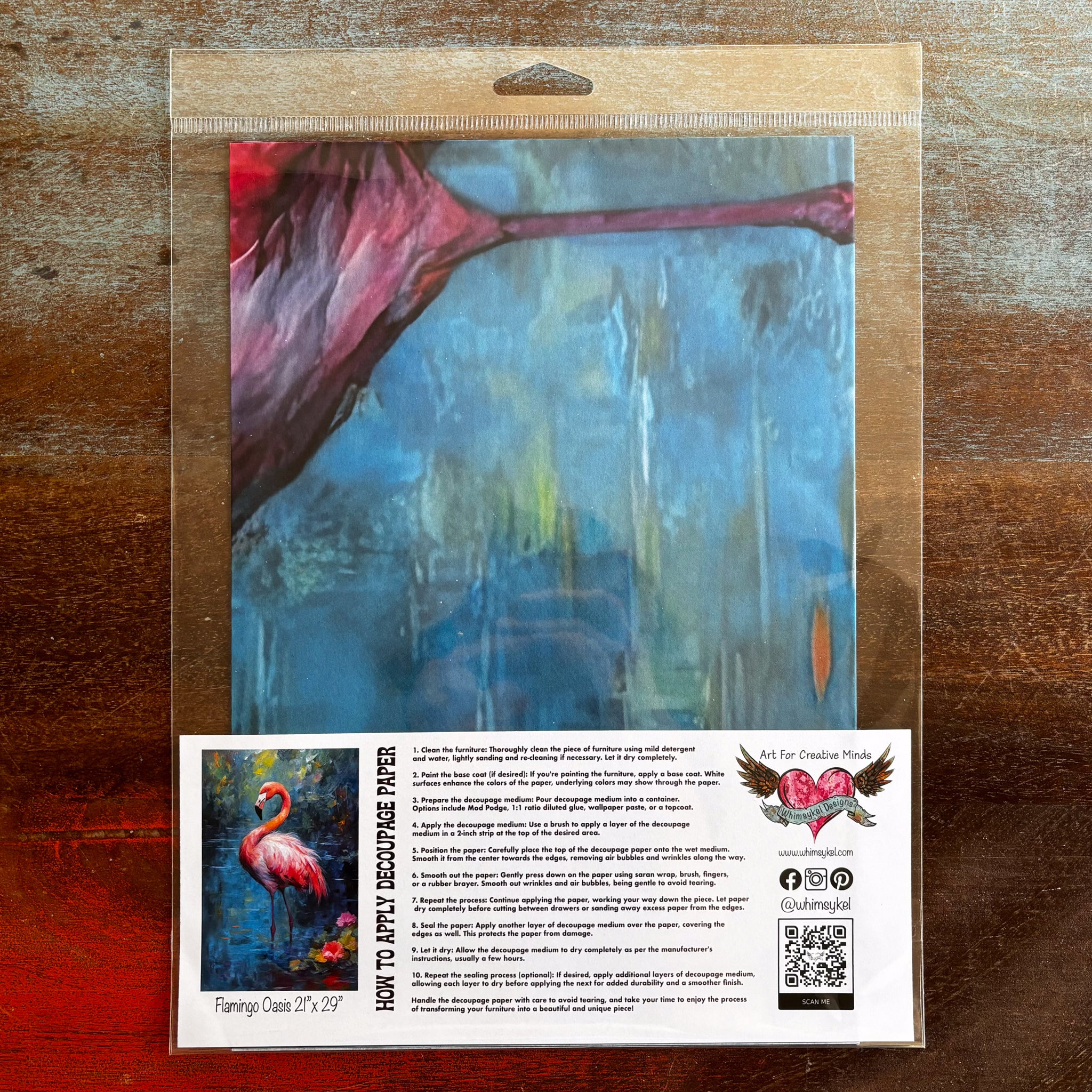 A package of Whimsykel's Flamingo Oasis tissue paper is against a dark wood background.