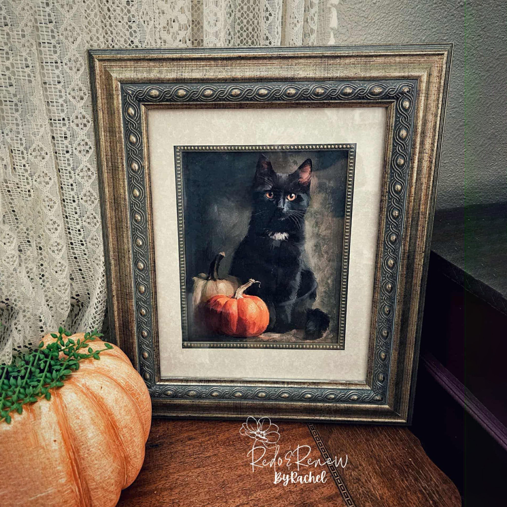 Framed portrait of a black cat with pumpkins on a wooden surface.