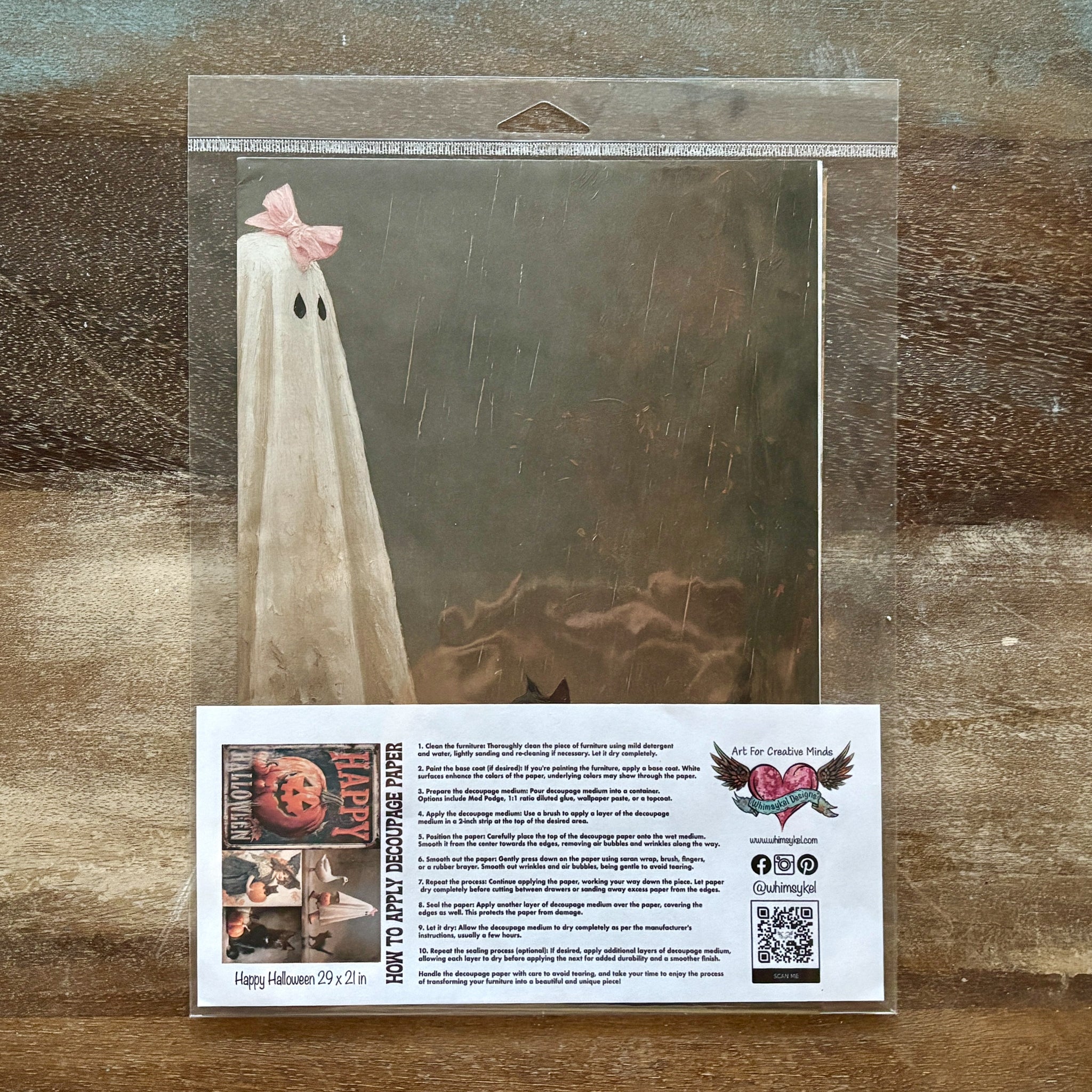 Ghost with a pink bow on a dark background, with a card below on a wooden surface