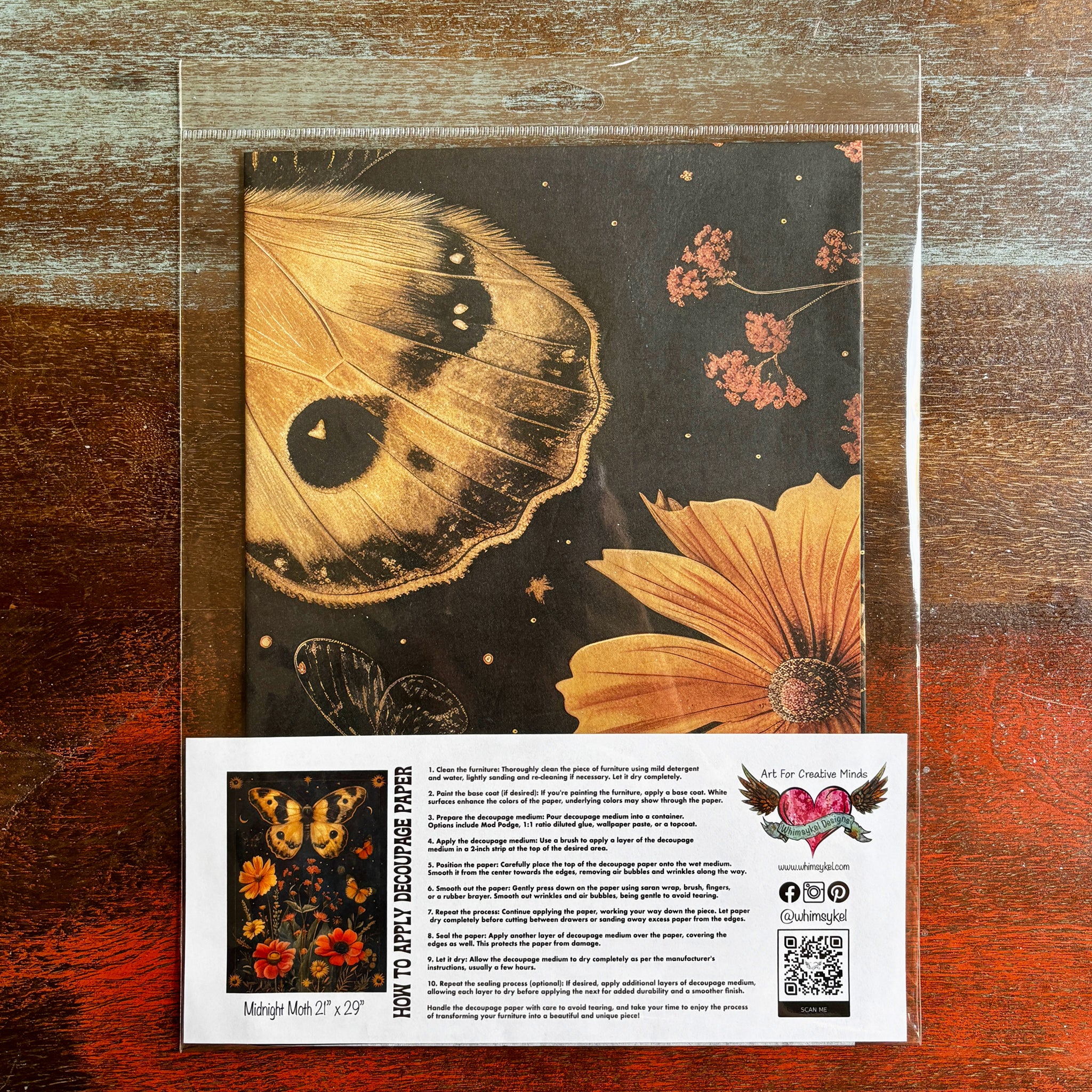 A package of Whimsykels Midnight Moth decoupage paper is against a dark wood background.