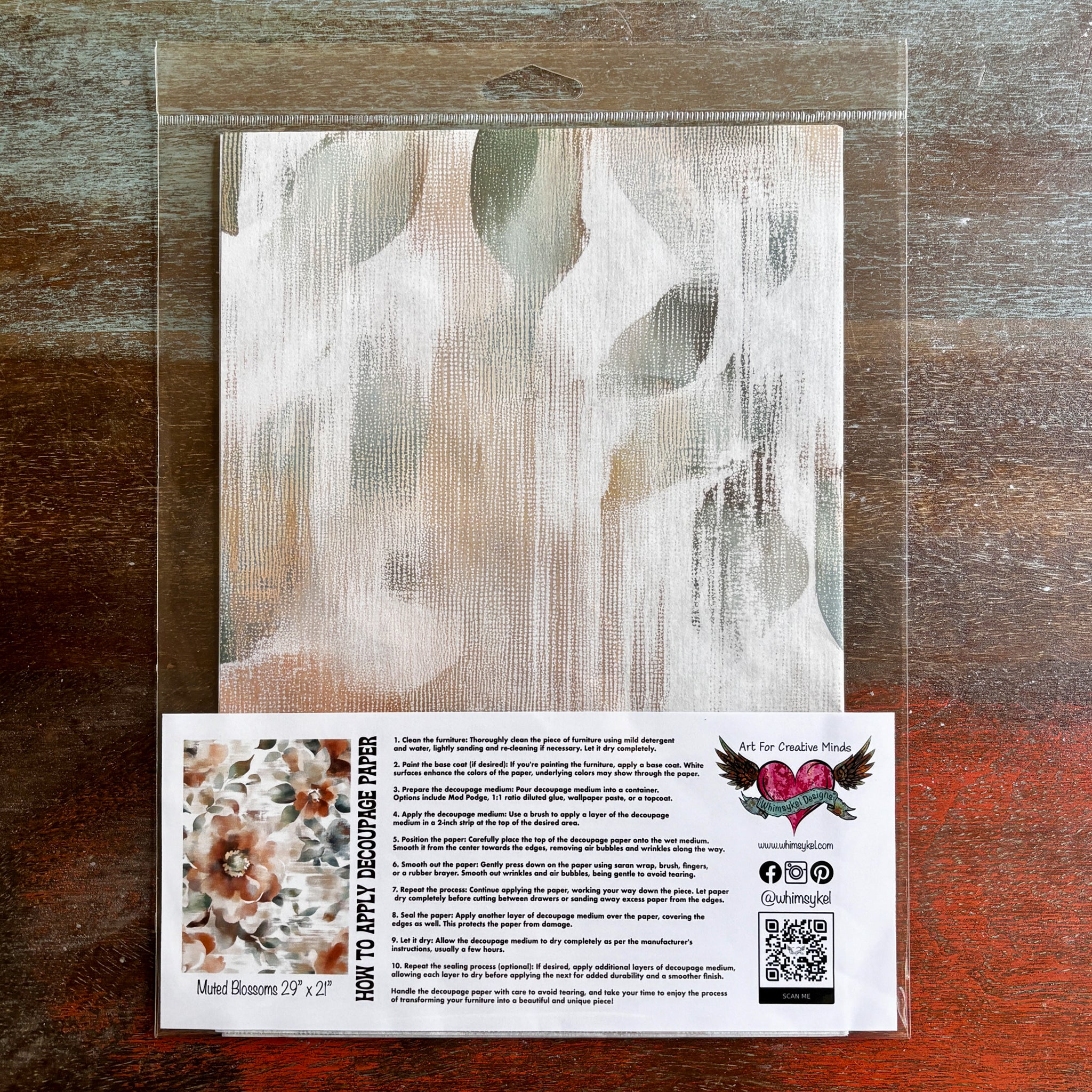 A package of Whimsykel's Muted Blossoms tissue paper is against a dark wood background.