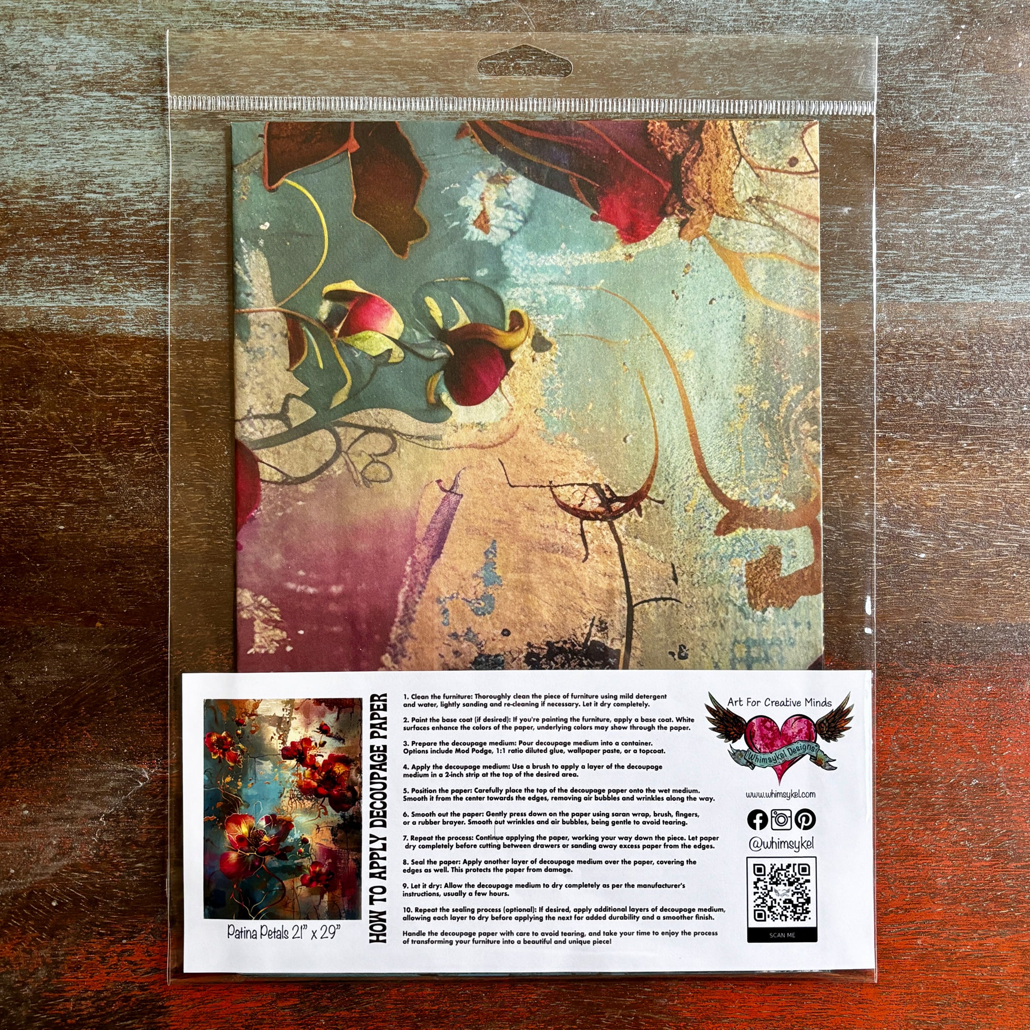 A package of Whimsykel's Patina Petals tissue paper is against a dark wood background.