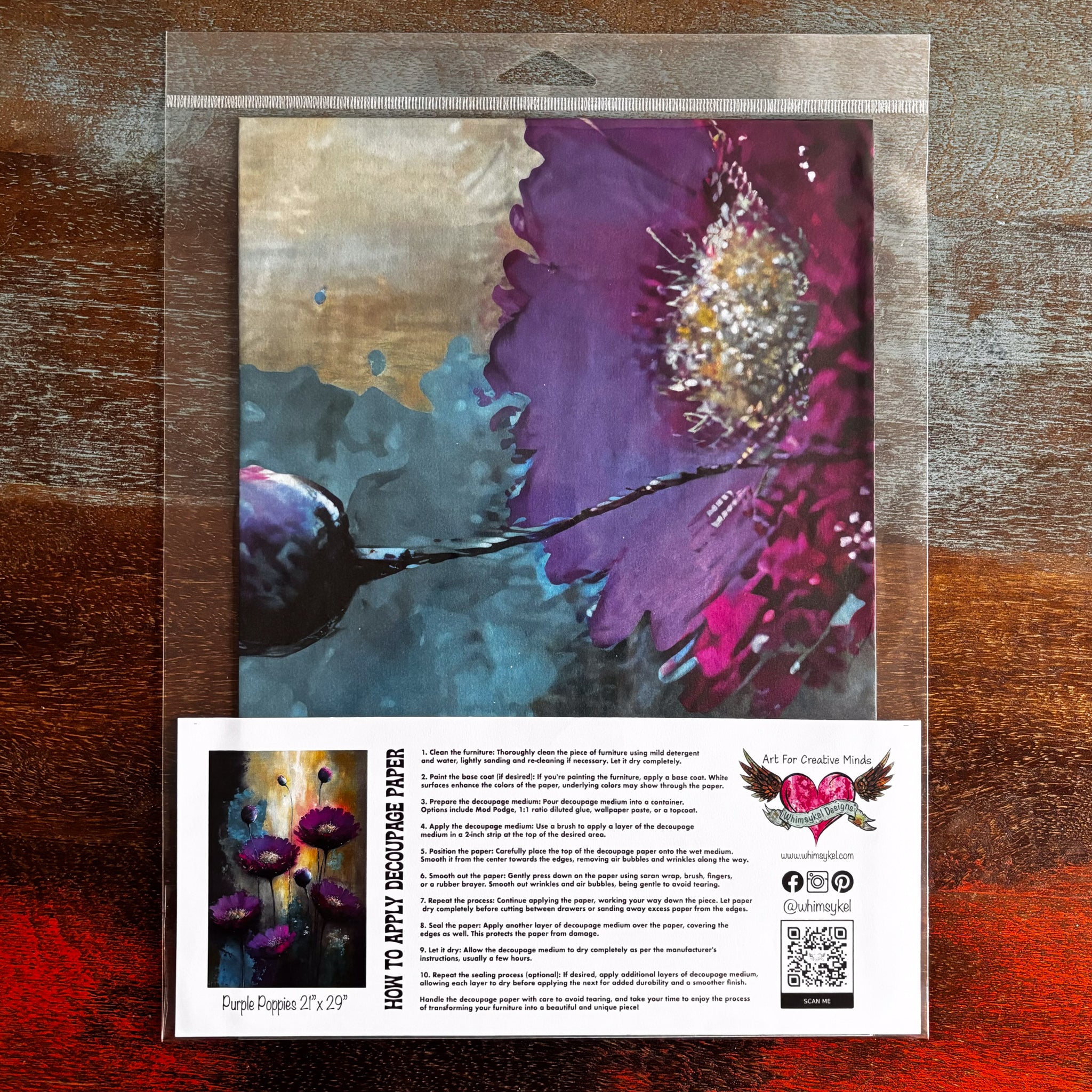 A package of Whimsykel's Purple Poppies tissue paper is against a dark wood background.