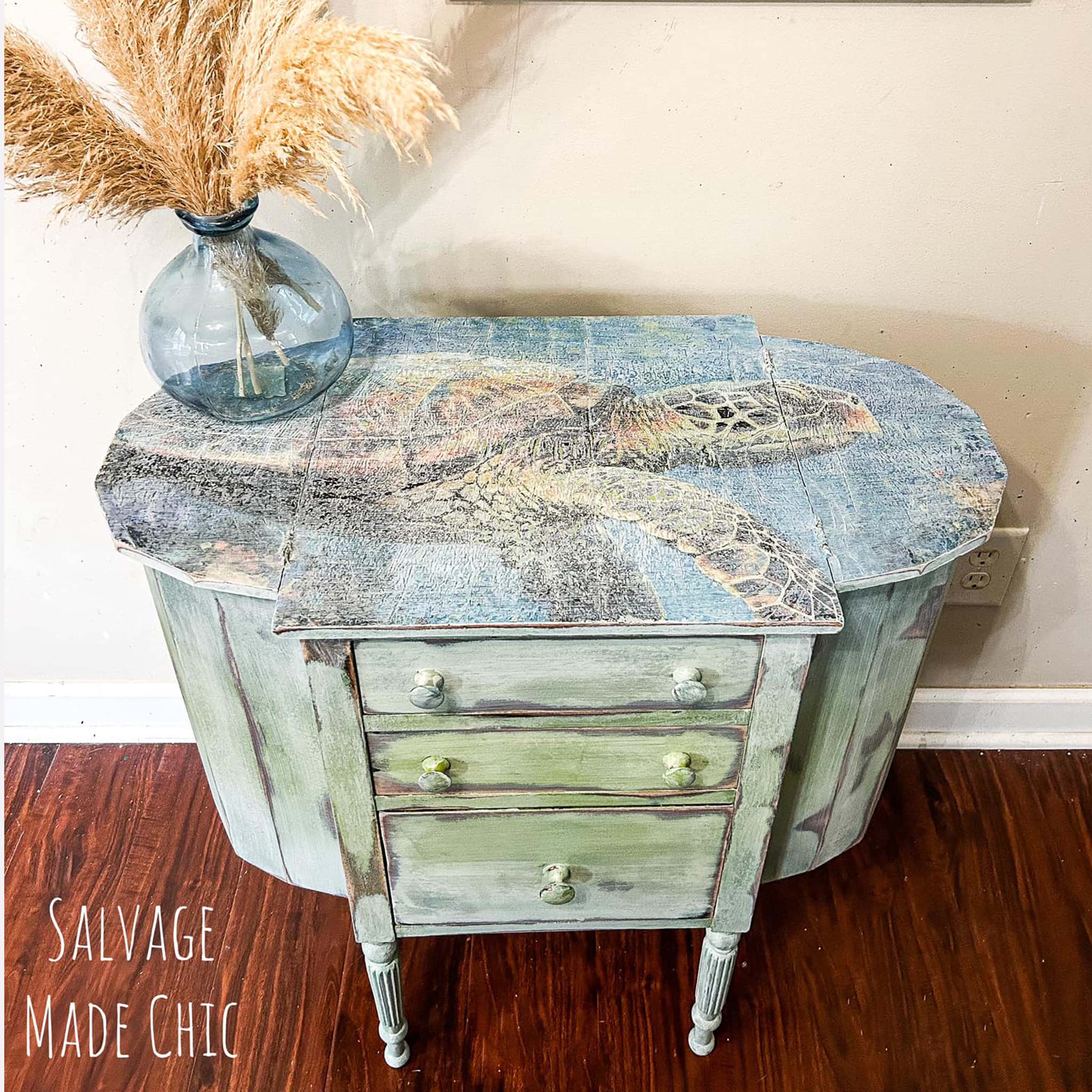 A vintage end table refurbished by Salvage Made Chic is painted a distressed pale green and features Whimsykel's Seymour tissue paper on the top. The tissue paper has been distressed as well.