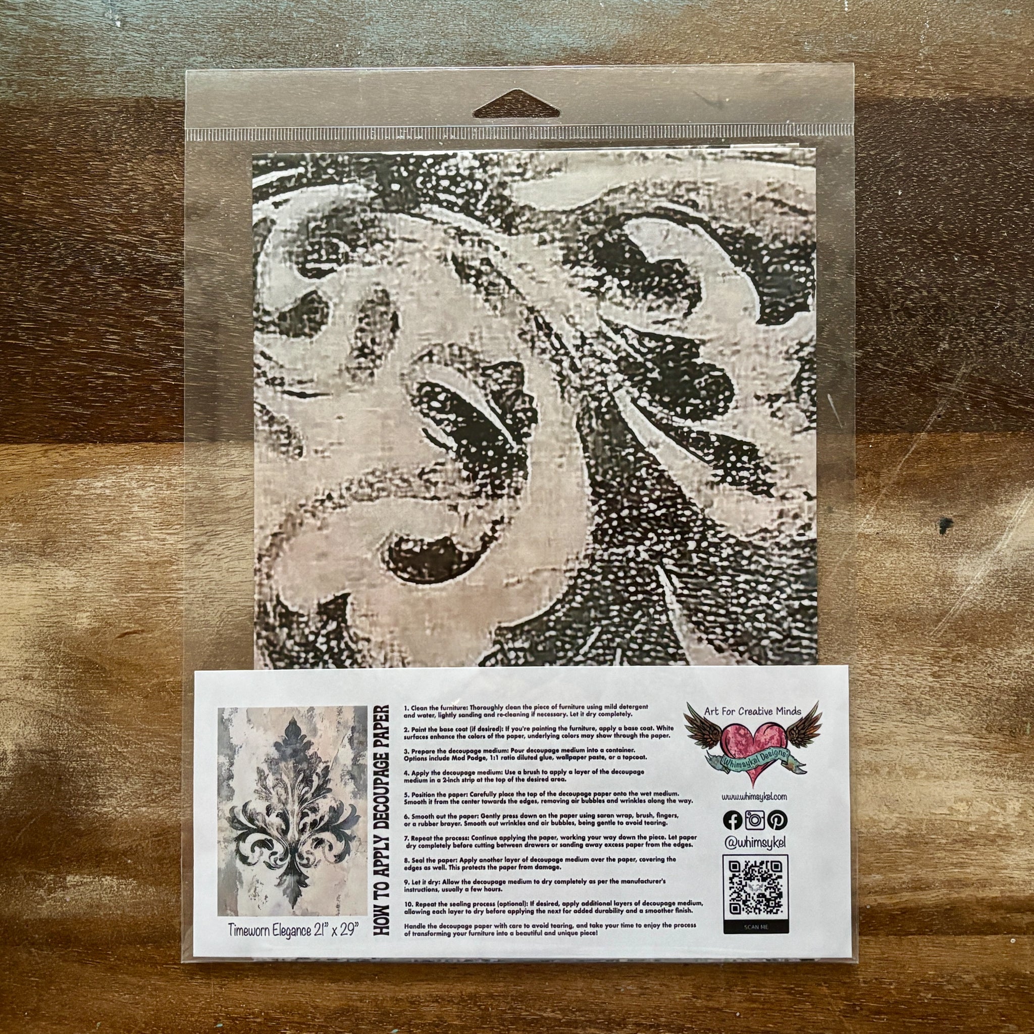 A package of Whimsykel's Timeworn Elegance tissue paper is against a wood background.