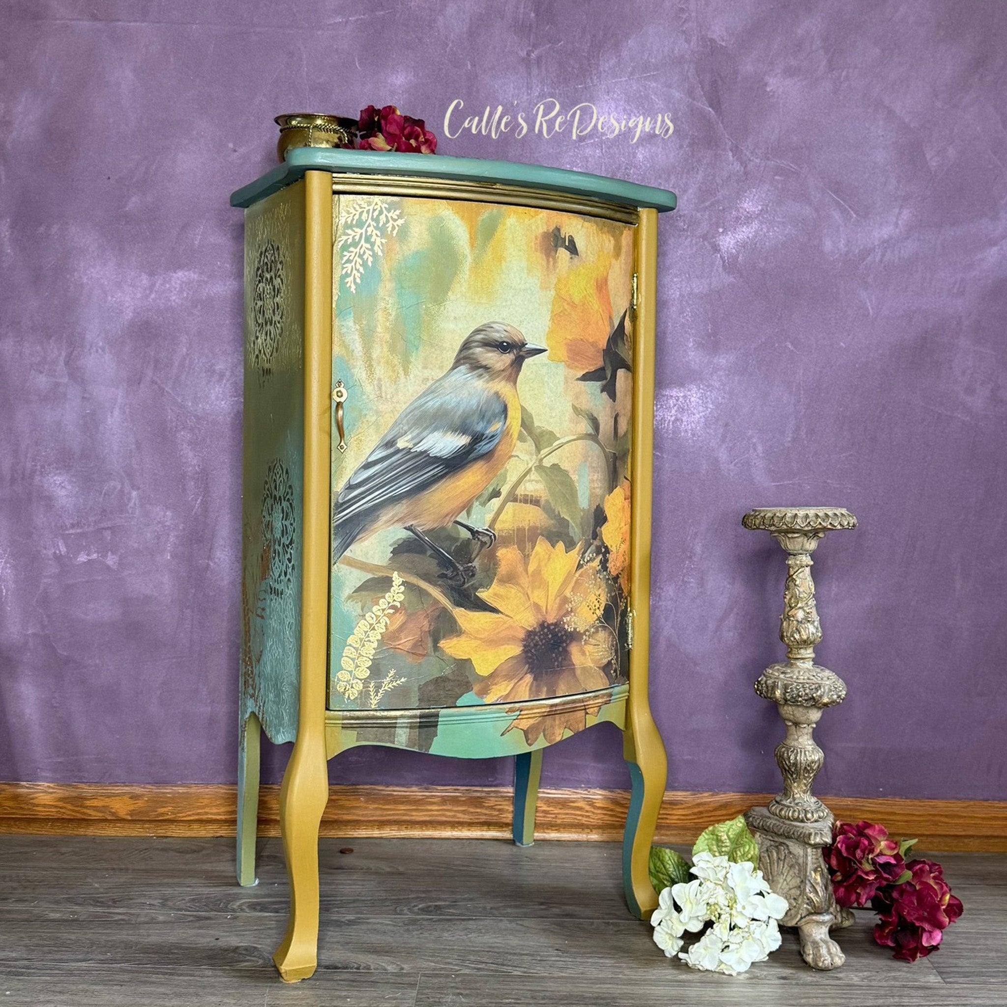 A small side table refurbished by Calle's ReDesigns is painted golden yellow with light green and features Whimsykel's October Bluebird tissue paper on its front door.