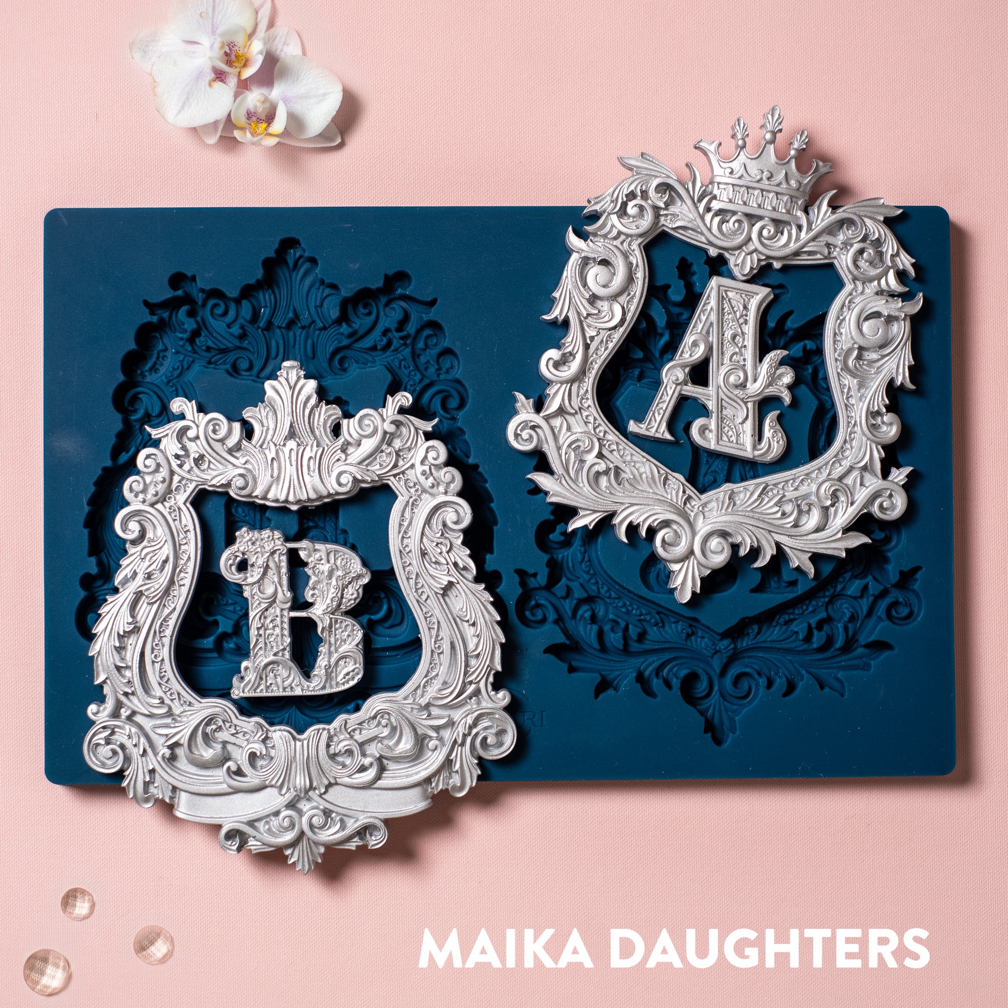 A blue silicone mold and silver colored castings of Zuri Design's A&B Monograms are against a light pink background.