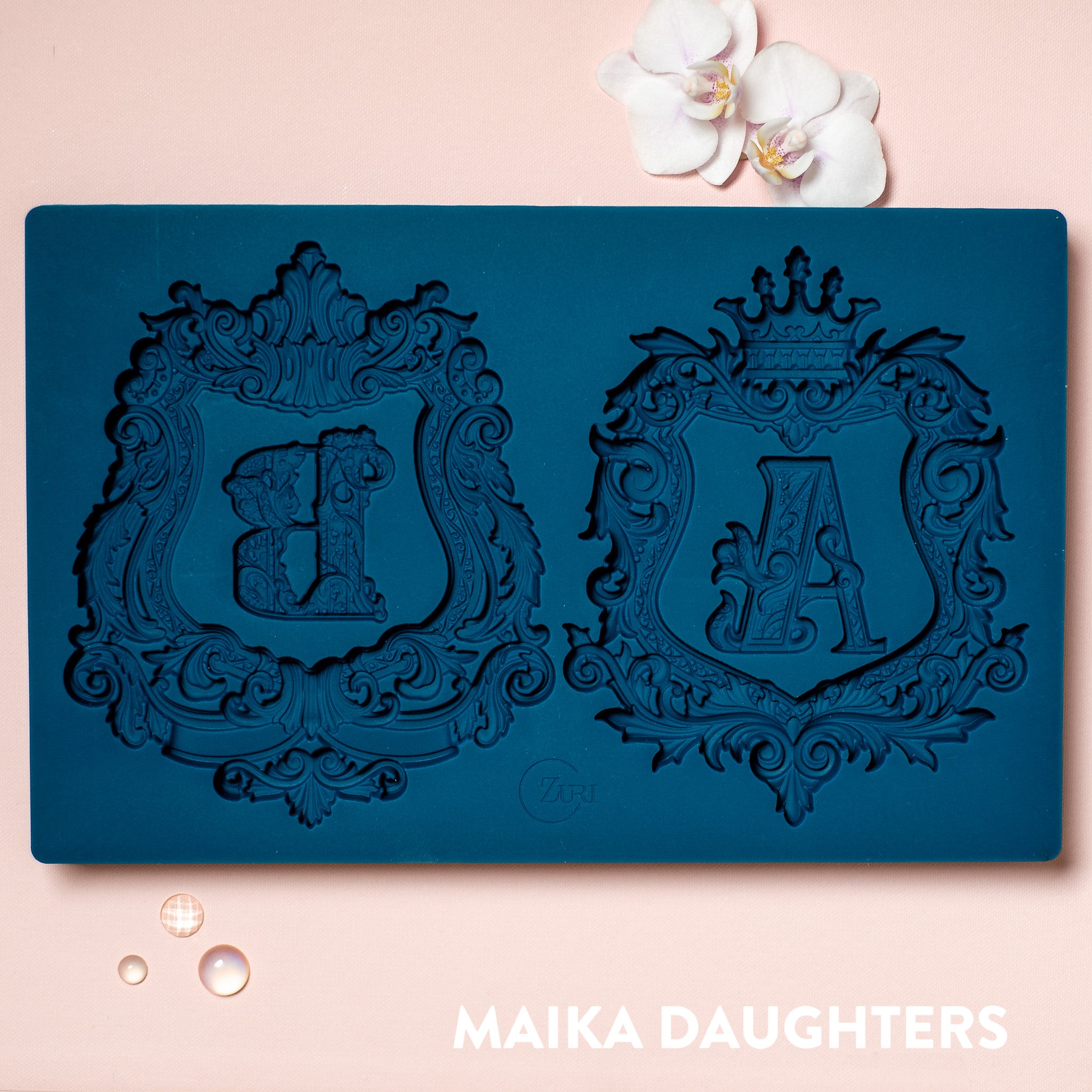 A blue silicone mold featuring 2 ornate letters of A&B and 2 ornate frames around them are against a light pink background.