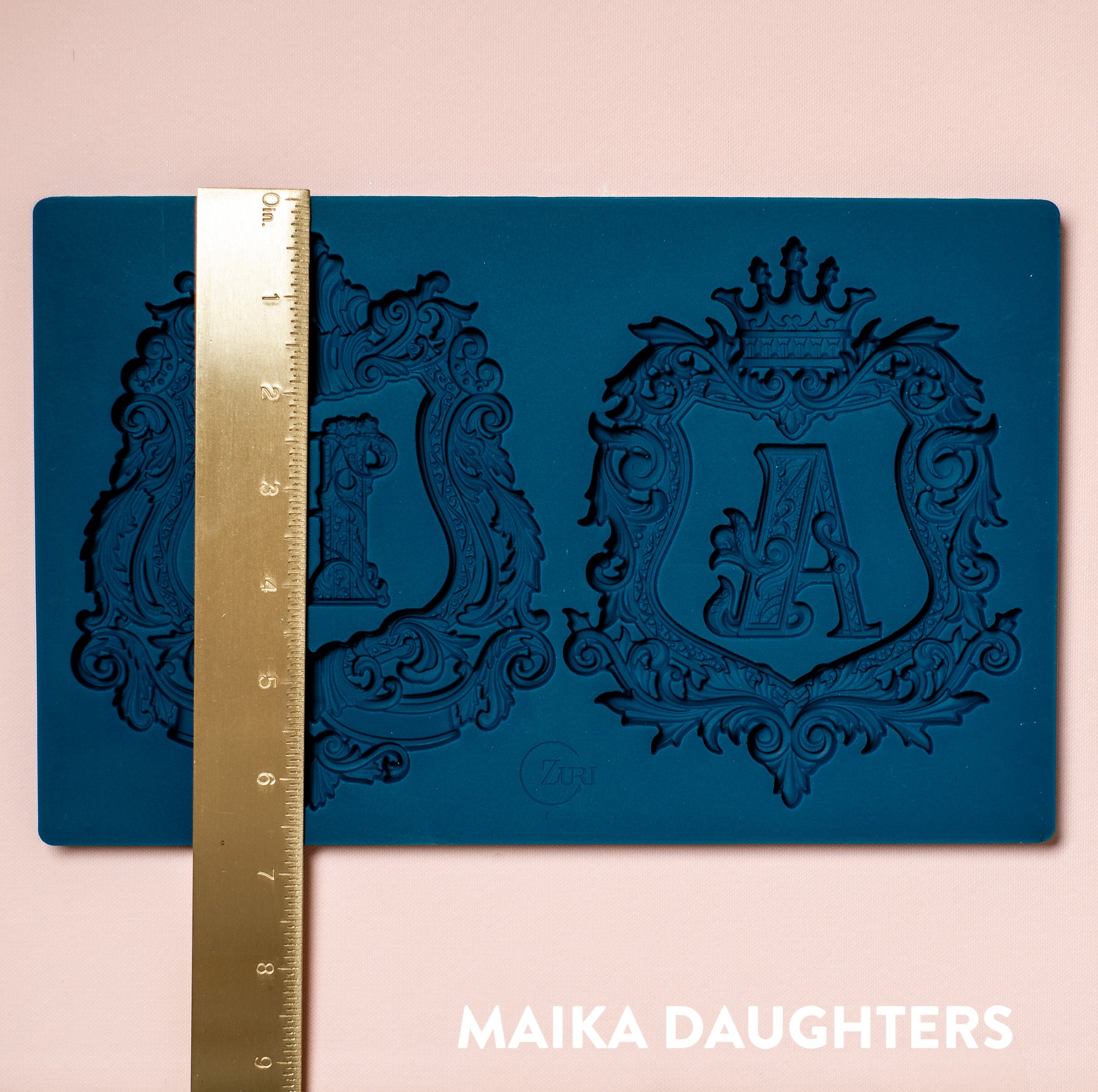 A blue silicone mold featuring 2 ornate letters of A&B and 2 ornate frames around them are against a light pink background. A gold ruler reading 6.8" height sits on the mold.