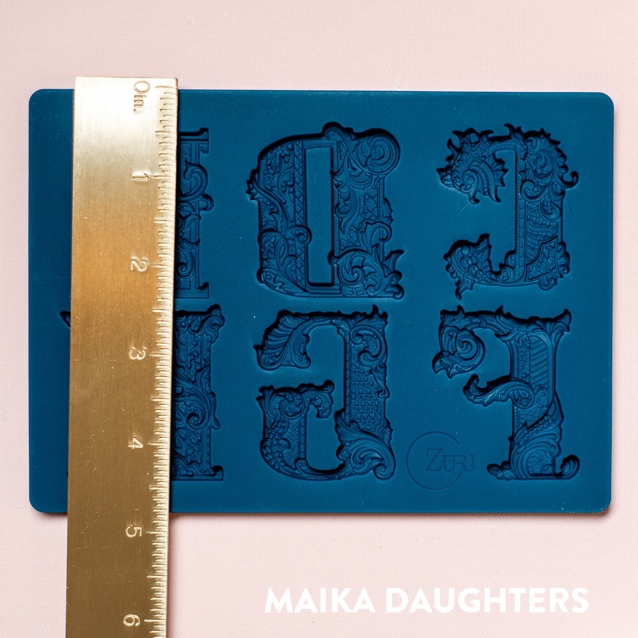 A blue silicone mold featuring 6 ornate letters of CDEFGH are against a light pink background. A gold ruler reading 4.88" height sits on the mold.