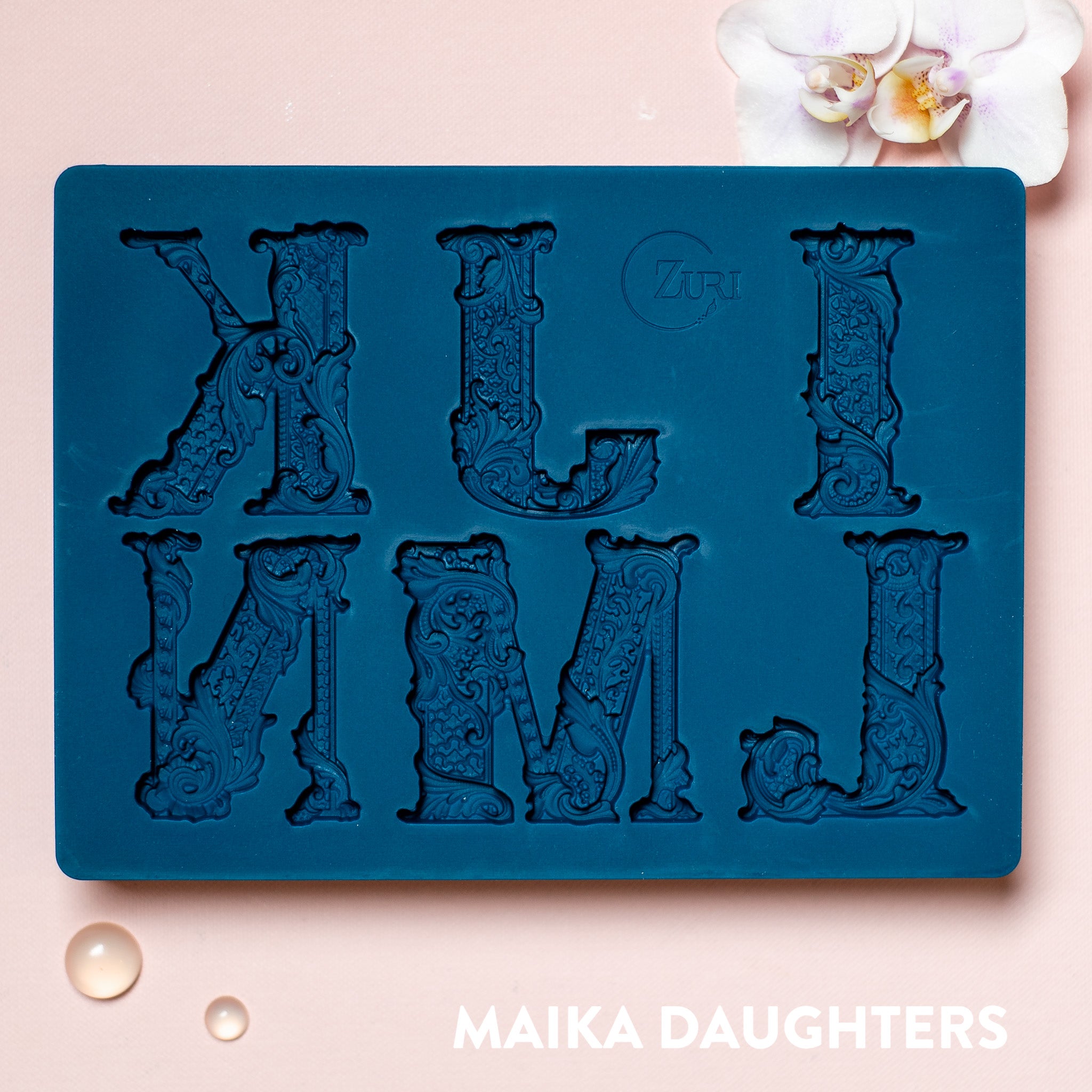 A blue silicone mold featuring 6 ornate letters of IJKLMN are against a light pink background.