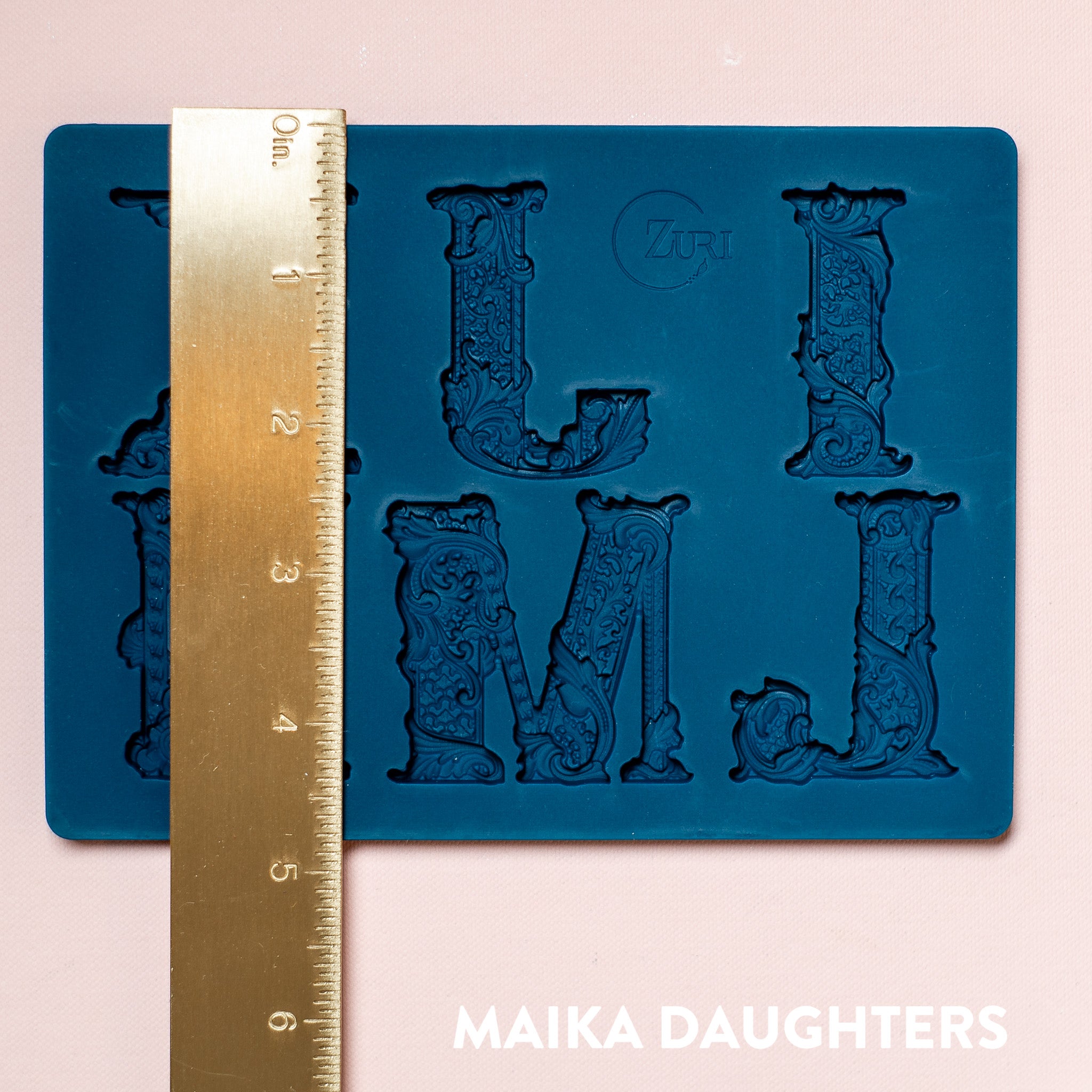 A blue silicone mold featuring 6 ornate letters of IJKLMN are against a light pink background. A gold ruler reading 4.88" height sits on the mold.