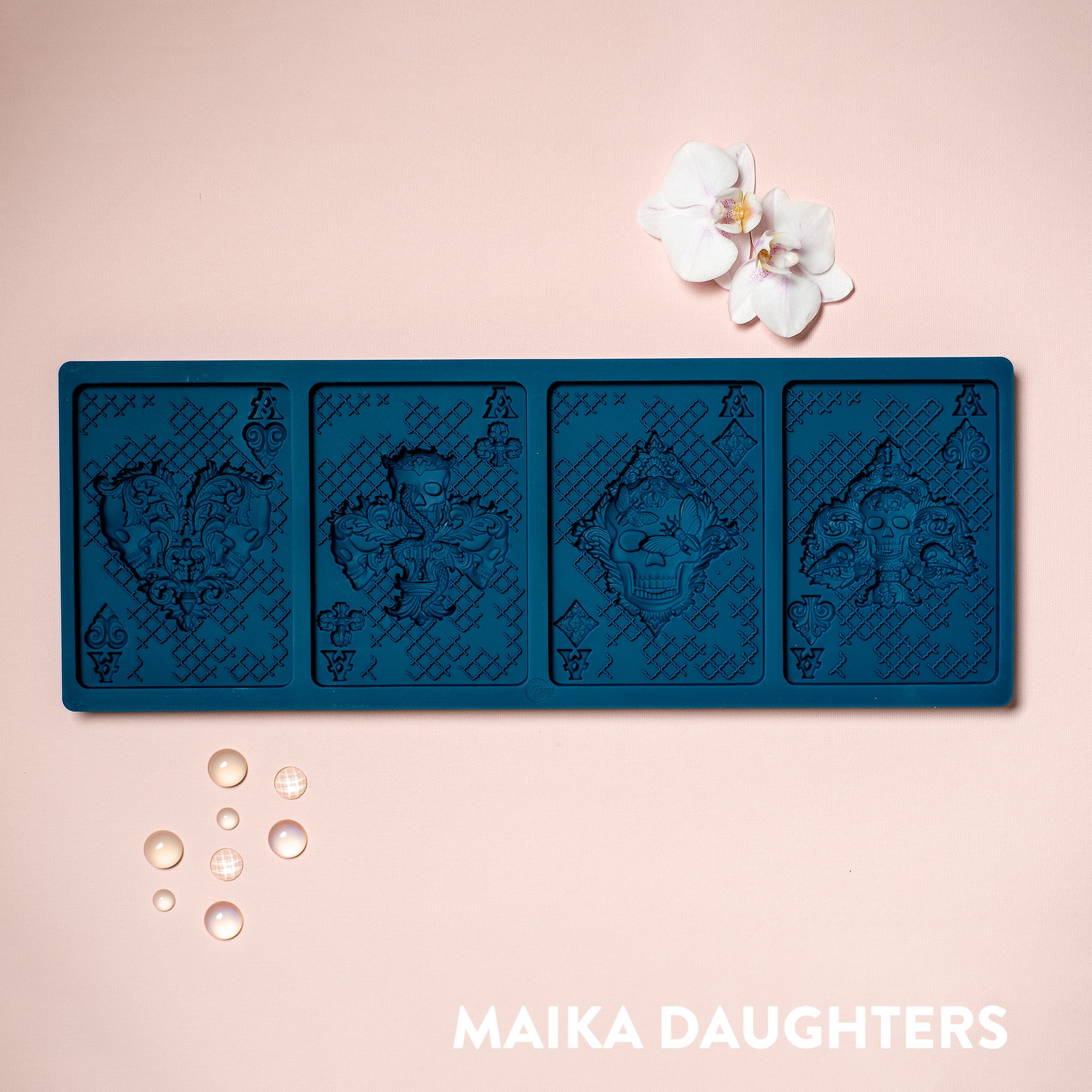 A blue silicone mold  of 4 ace playing cards with skulls is against a light pink background.