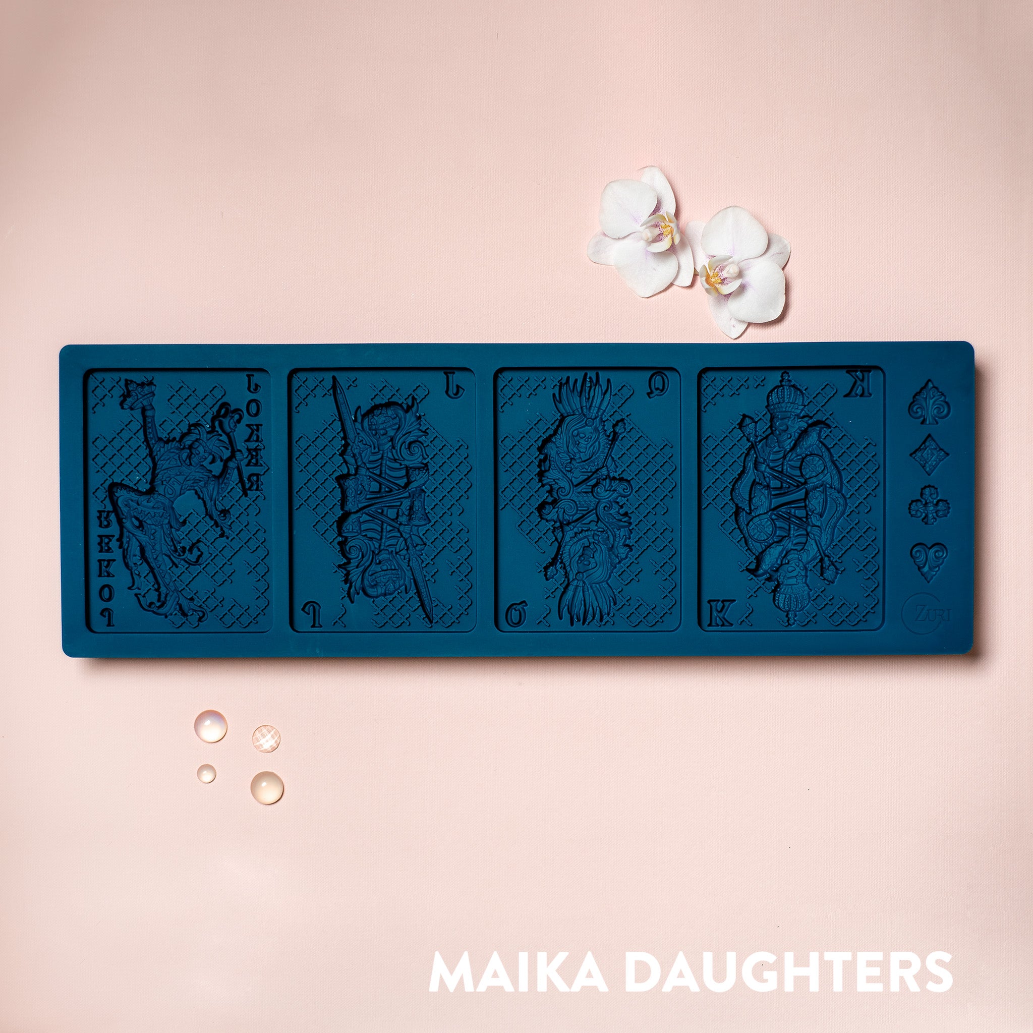 A blue silicone mold of 4 playing cards that feature a king, queen, jack, and joker with skeleton face designs is against a light pink background.