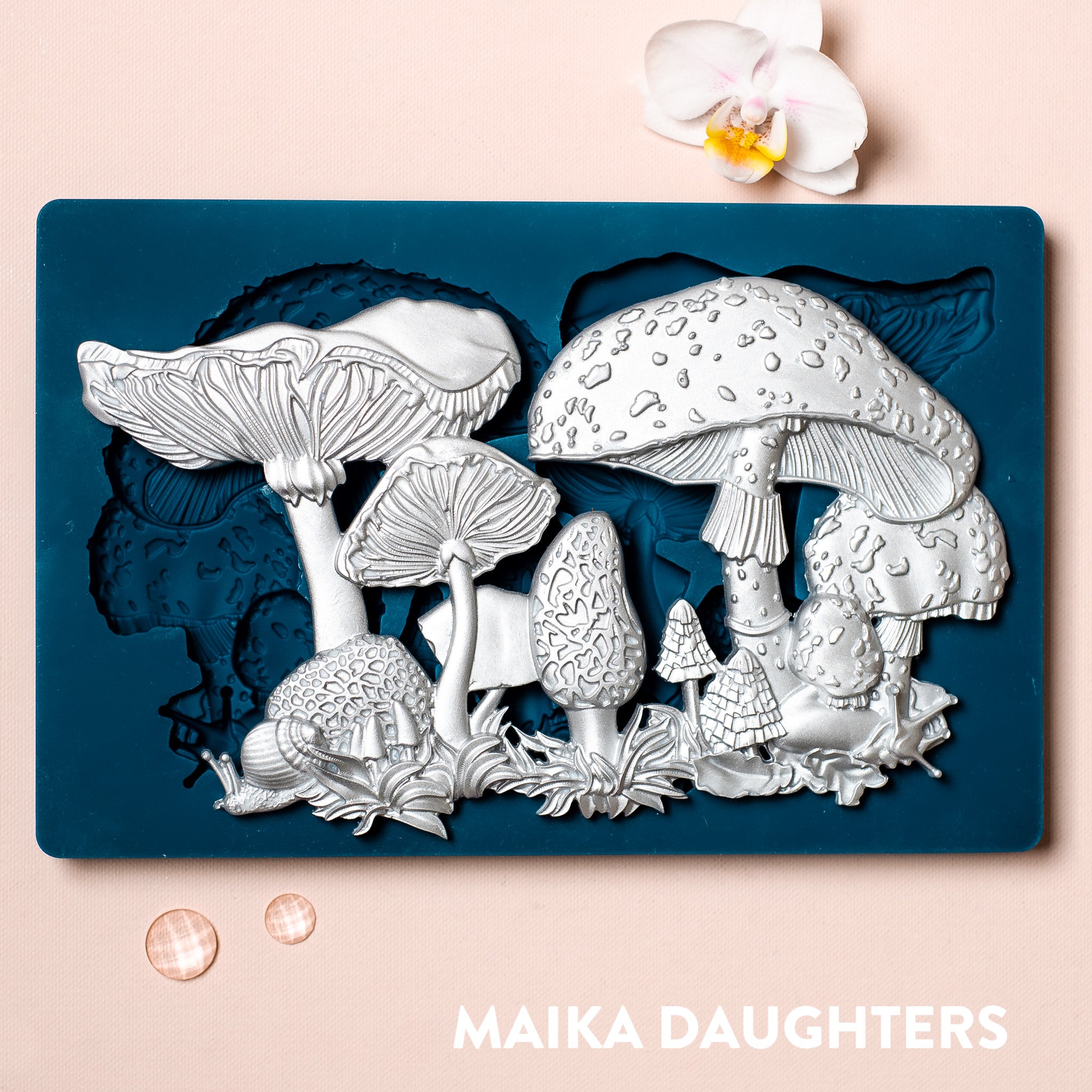 A blue silicone mold and silver colored castings of Zuri Design's Fairyland Mushrooms are against a light pink background.