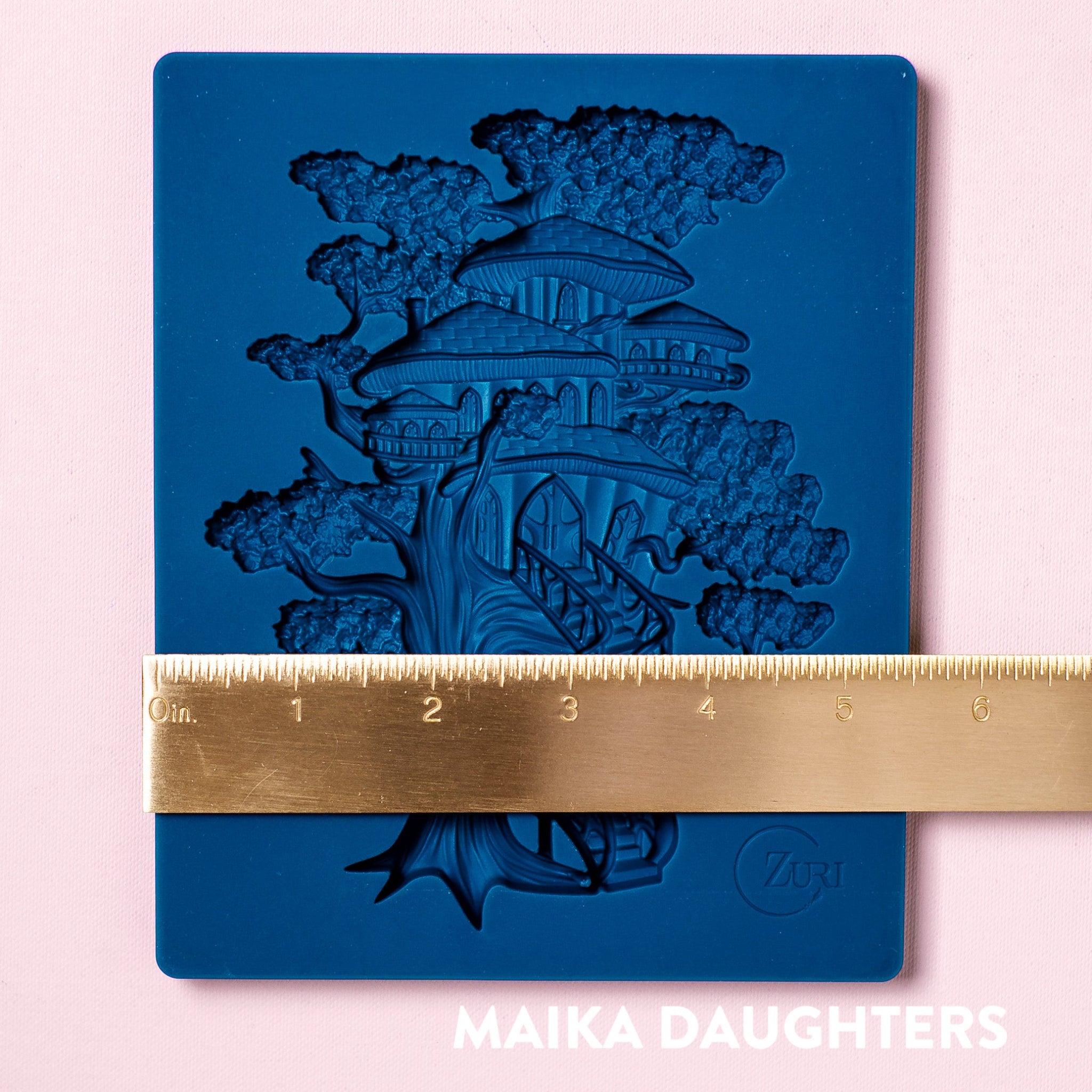 A blue silicone mold of a tree house  made of mushrooms is against a light pink background. A gold ruler reading 5.5" width sits on the mold.