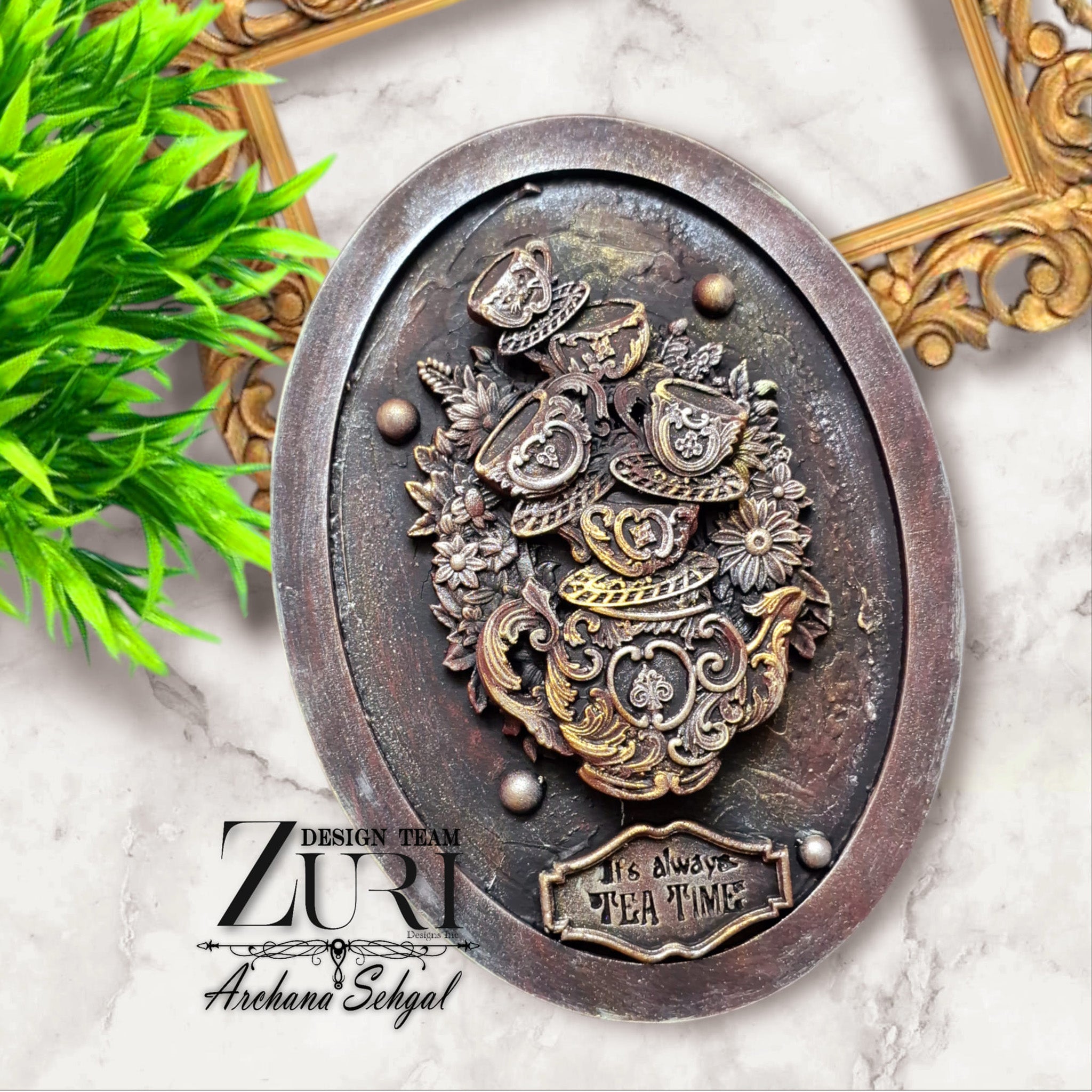 An oval plate decor created by Archana Sehgal is painted to look like vintage metal and features a casting of Zuri Design's Tea Time silicone mold in the center.