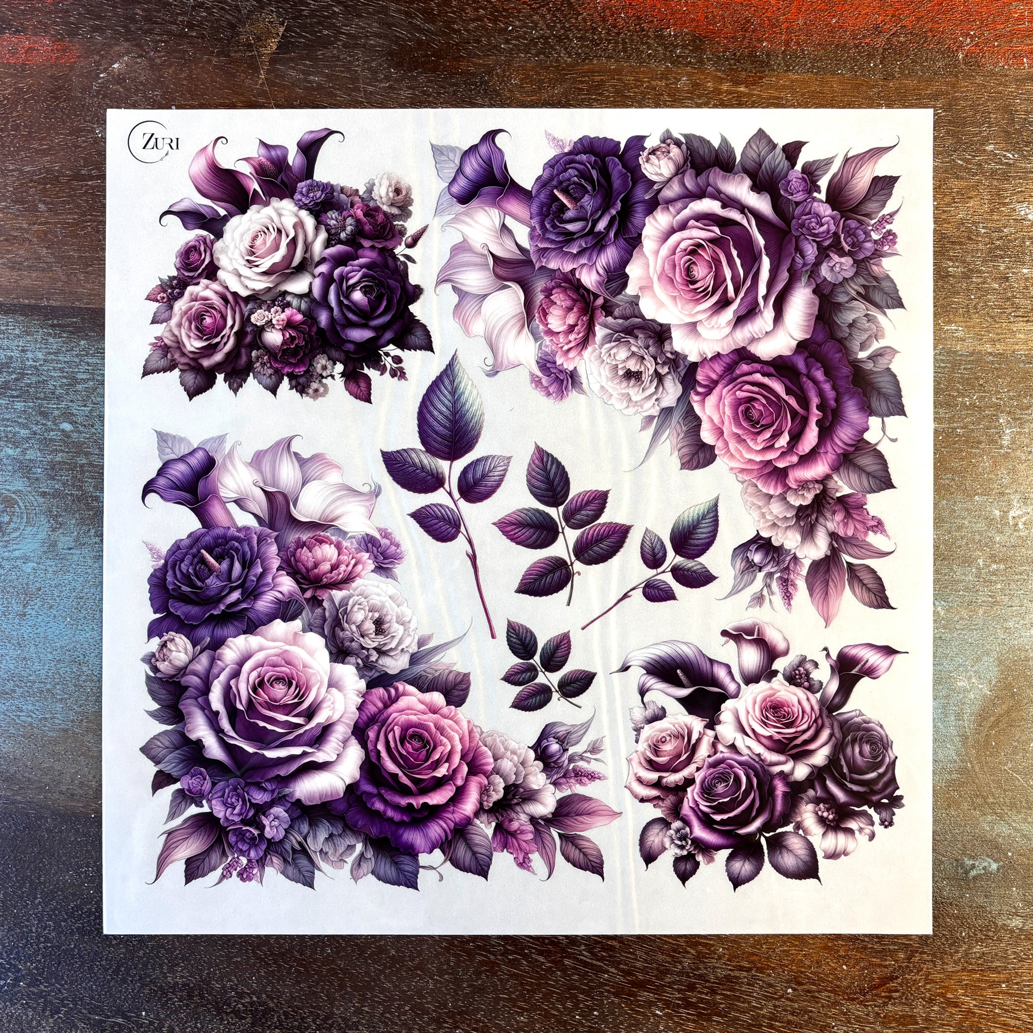 A sheet of small rub-on transfers featuring small bouquets of roses and lilies in pinks and purples is against a dark wood background.