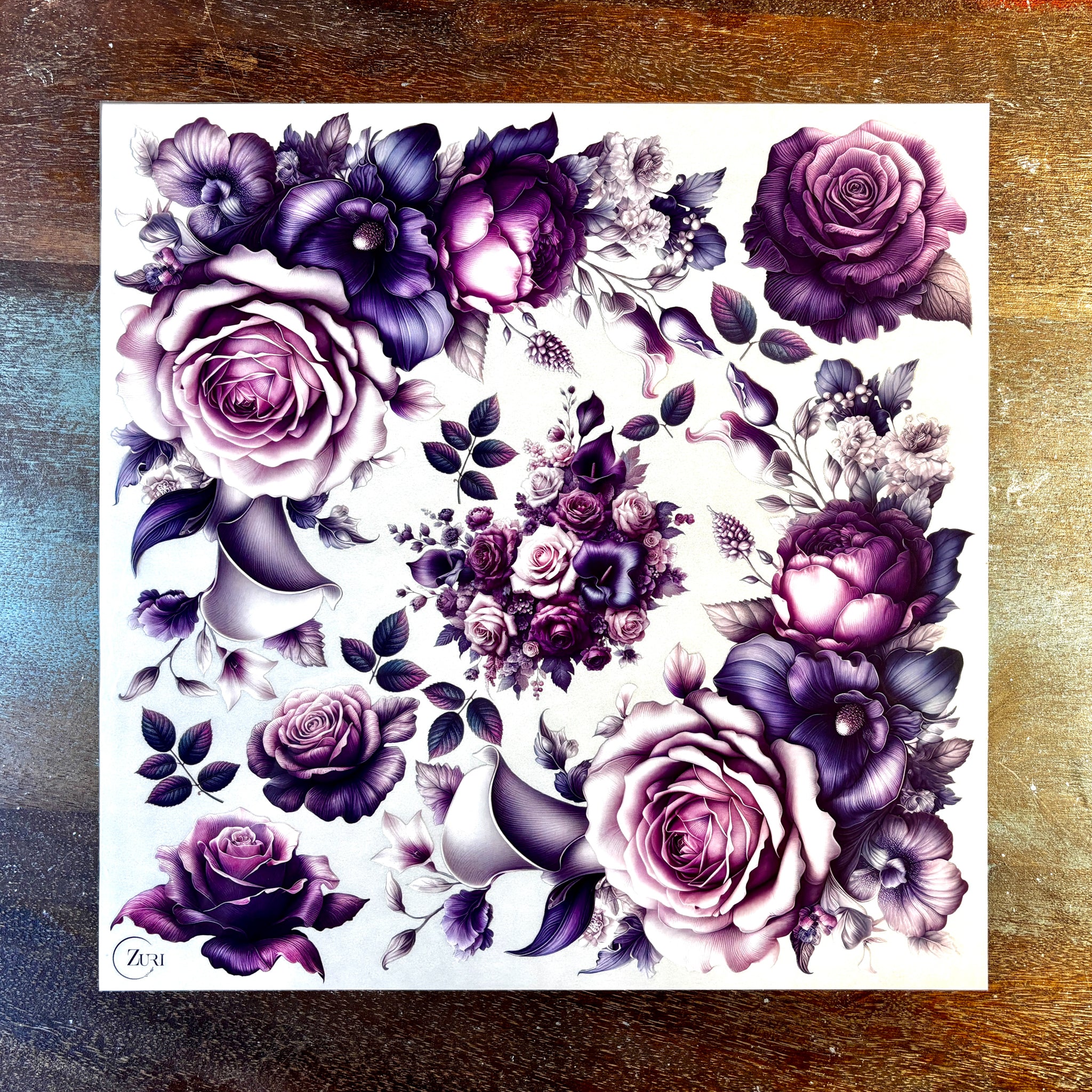 A sheet of small rub-on transfers featuring small bouquets and single blooms of roses and lilies in pinks and purples is against a dark wood background.