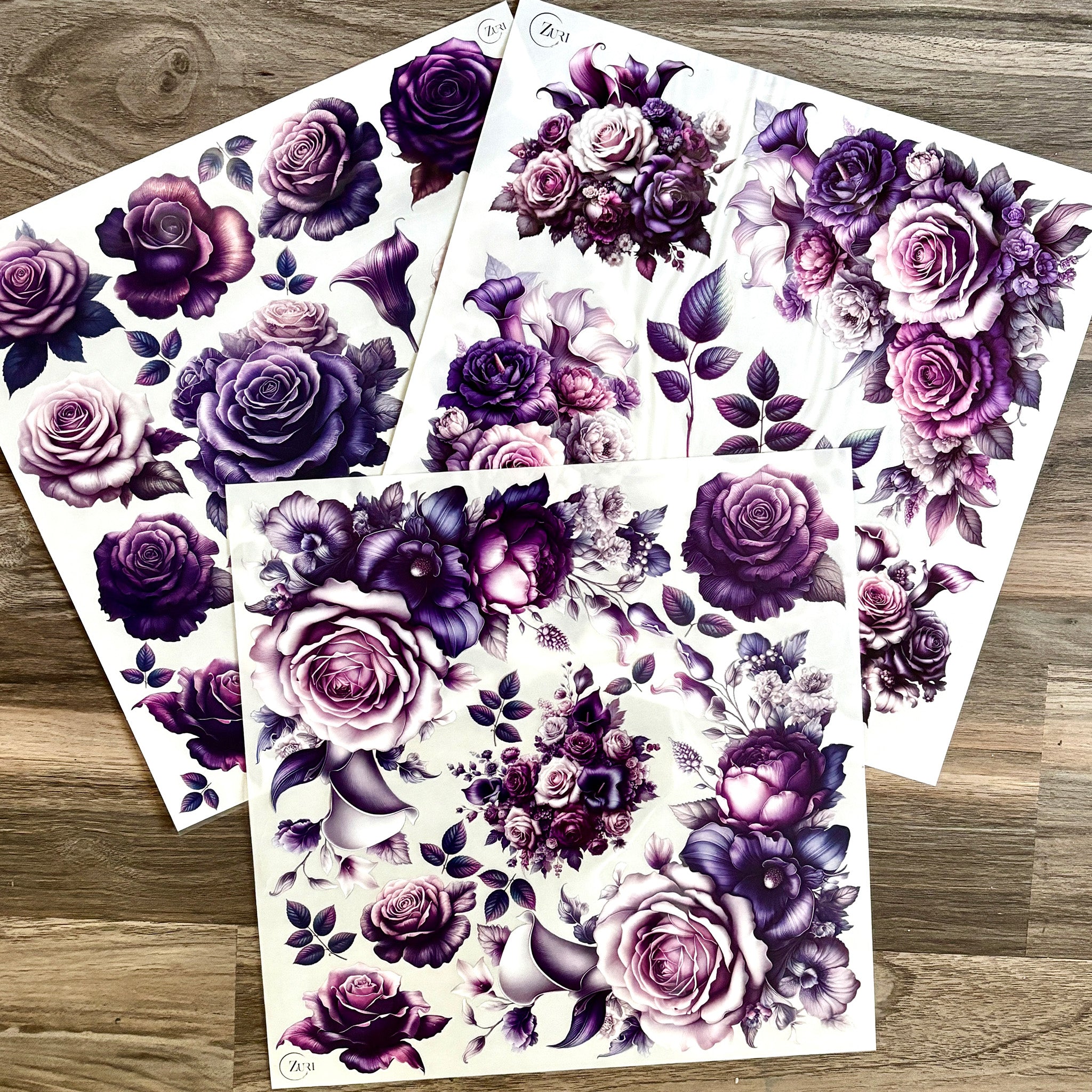 Three sheets of small rub-on transfers featuring pink and purple roses and lilies are against a wood background.