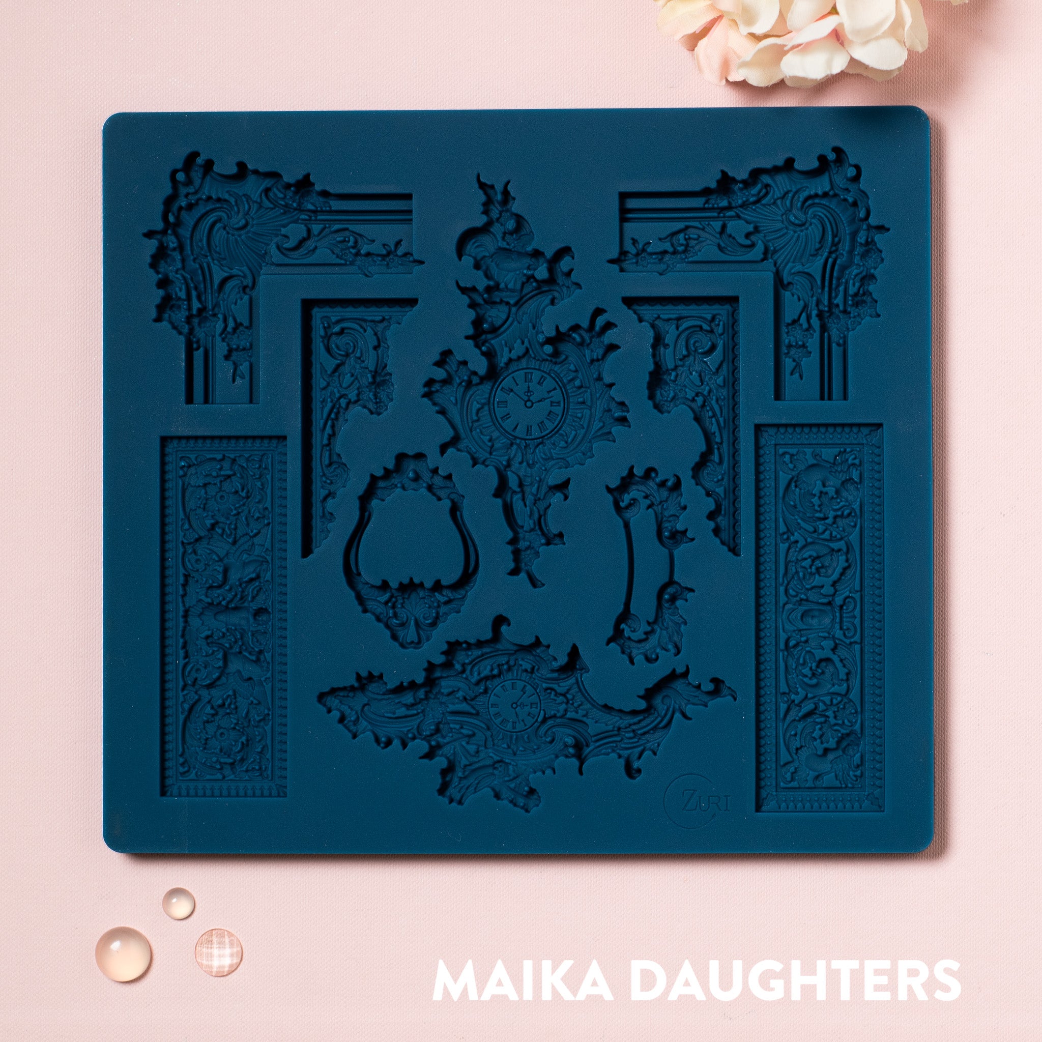 A blue silicone mold featuring 10 pieces of ornate frame corners, borders, and center accent pieces are against a light pink background.