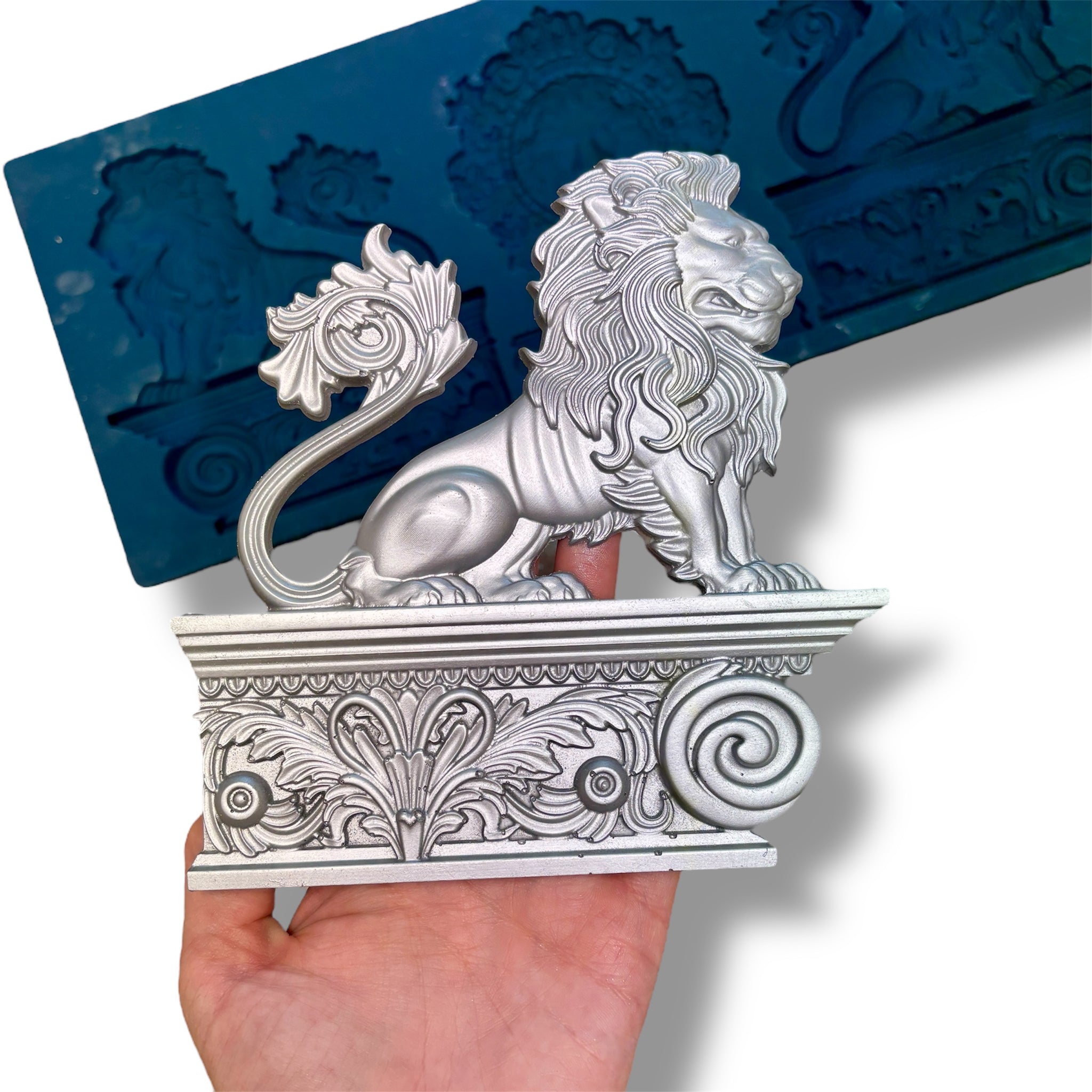 Zuri's Baroque Lions silicone mold is against a white background. A hand is shown holding one of the lion statue castings.