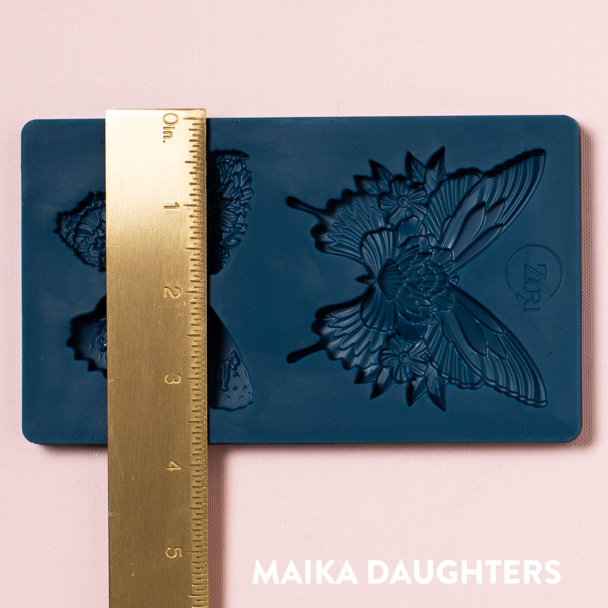 A blue silicone mold of 2 ornate floral butterflies is against a light pink background. A gold ruler reading 3.75" height sits on the mold.